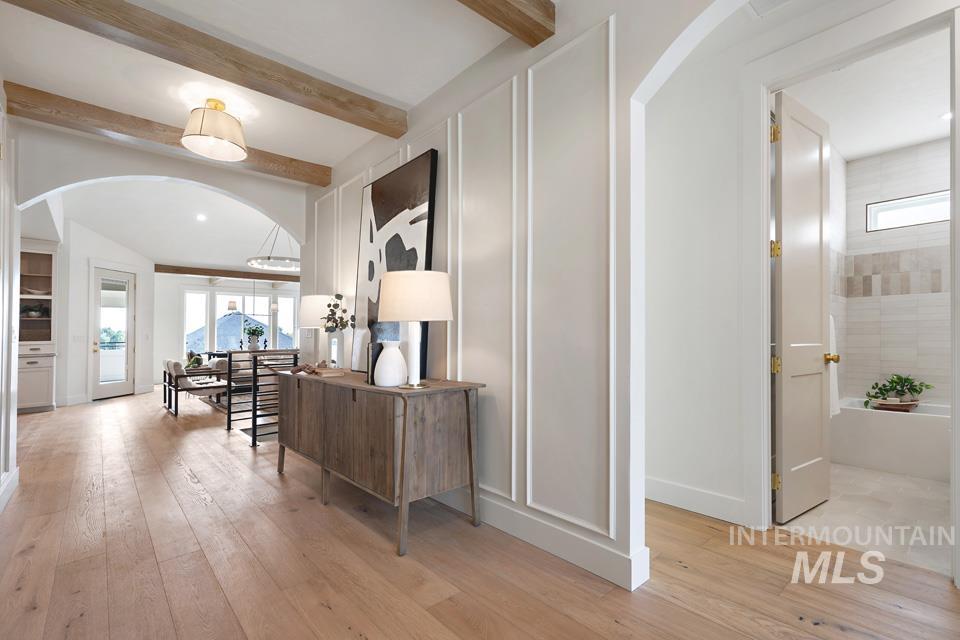 Hall with arched walkways, light wood-style floors, and beam ceiling