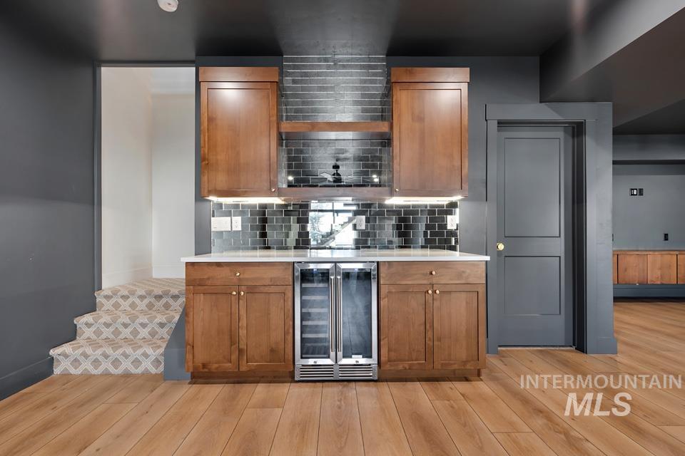 Bar area featuring brown cabinetry, beverage cooler, open shelves, and light wood-type flooring