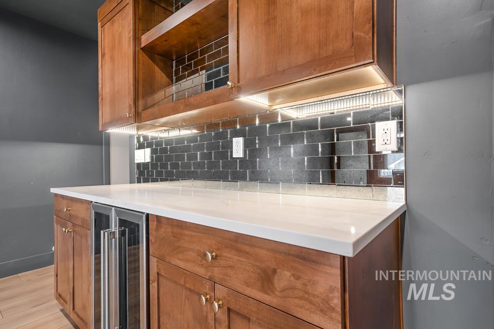 Kitchen featuring brown cabinetry, beverage cooler, tasteful backsplash, light stone counters, and light wood-type flooring