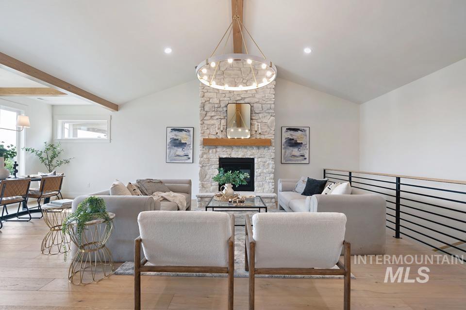 Living area featuring beamed ceiling, light wood-style floors, a stone fireplace, and high vaulted ceiling