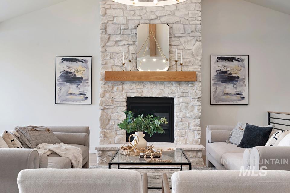 Living area with vaulted ceiling, a stone fireplace, and wood finished floors