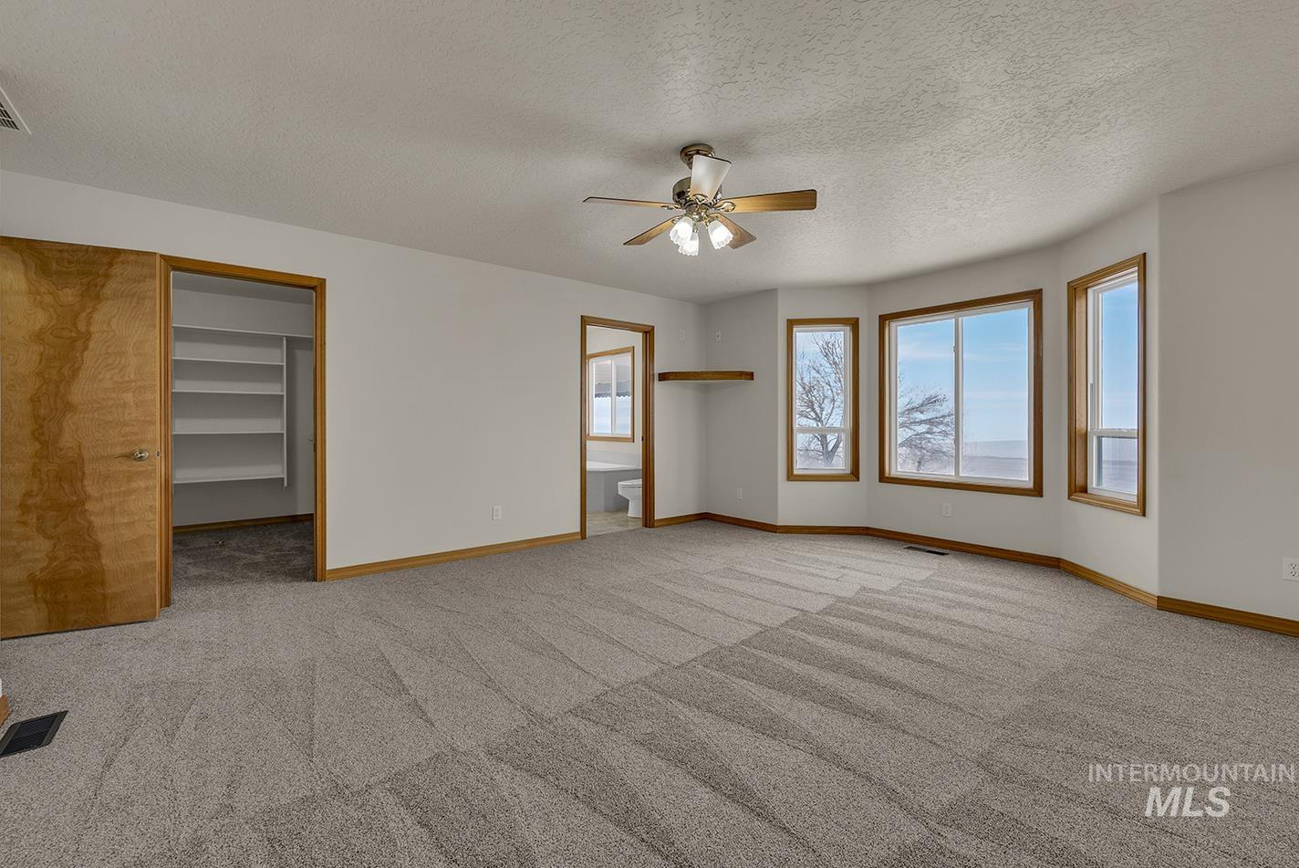 Unfurnished bedroom featuring a walk in closet, a textured ceiling, ceiling fan, ensuite bathroom, and light carpet