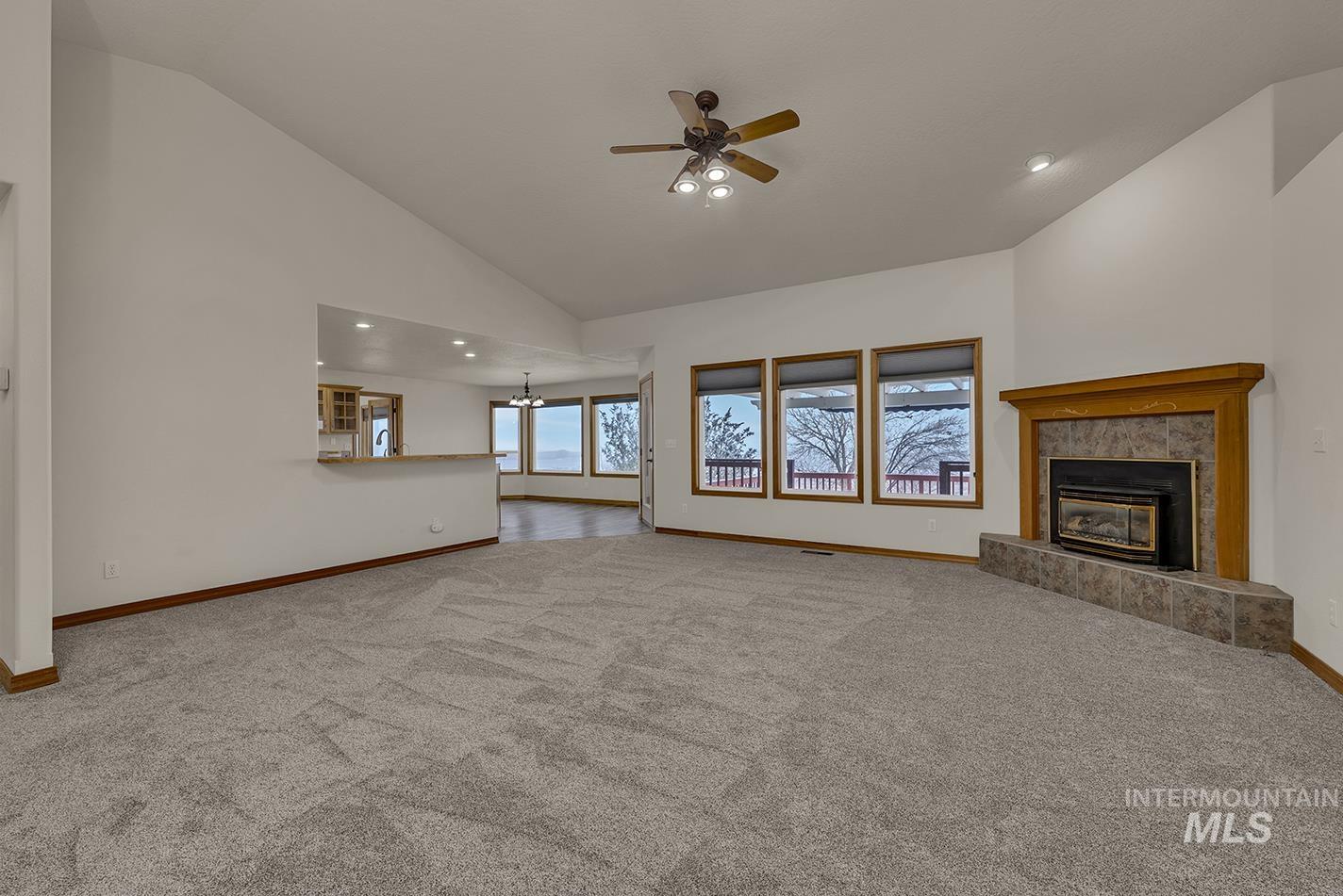 Unfurnished living room featuring a tiled fireplace, light carpet, recessed lighting, ceiling fan, and a chandelier