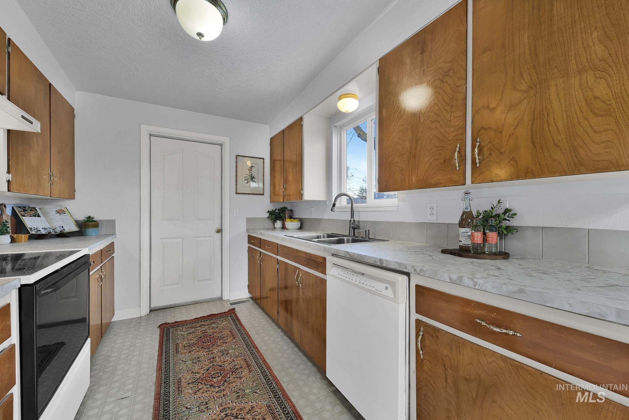 Kitchen featuring light floors, brown cabinetry, dishwasher, electric stove, and light countertops