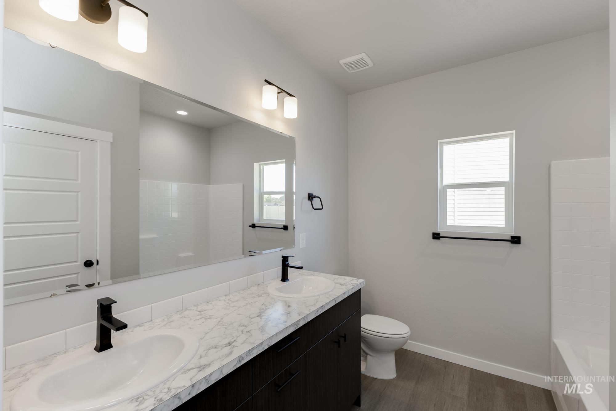 Full bathroom with double vanity, dark wood-style flooring, and  shower combination