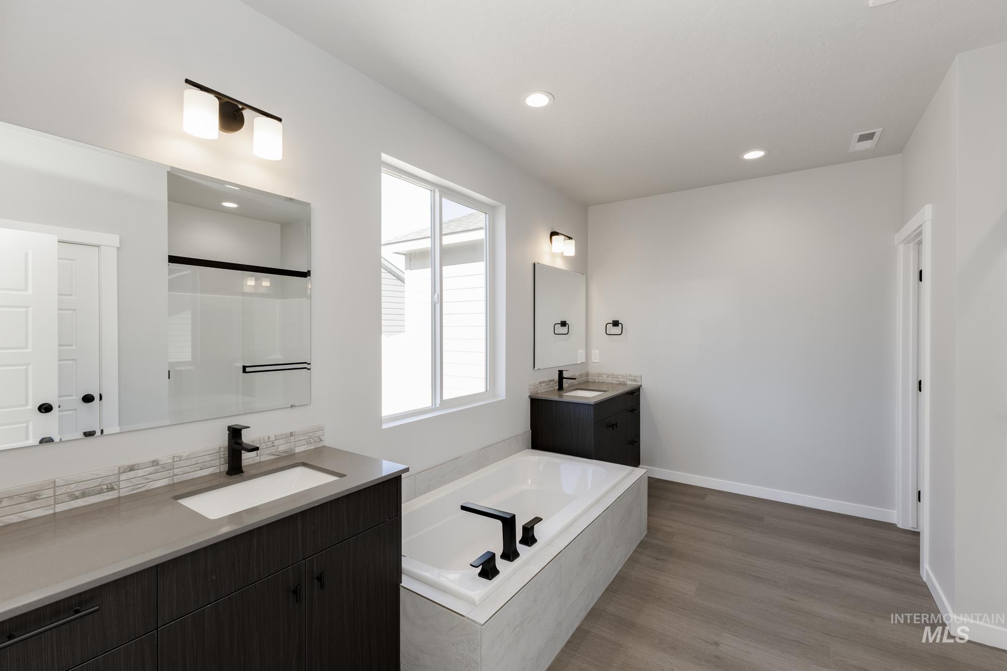 Full bathroom featuring two vanities, a bath, a shower stall, light wood-type flooring, and recessed lighting