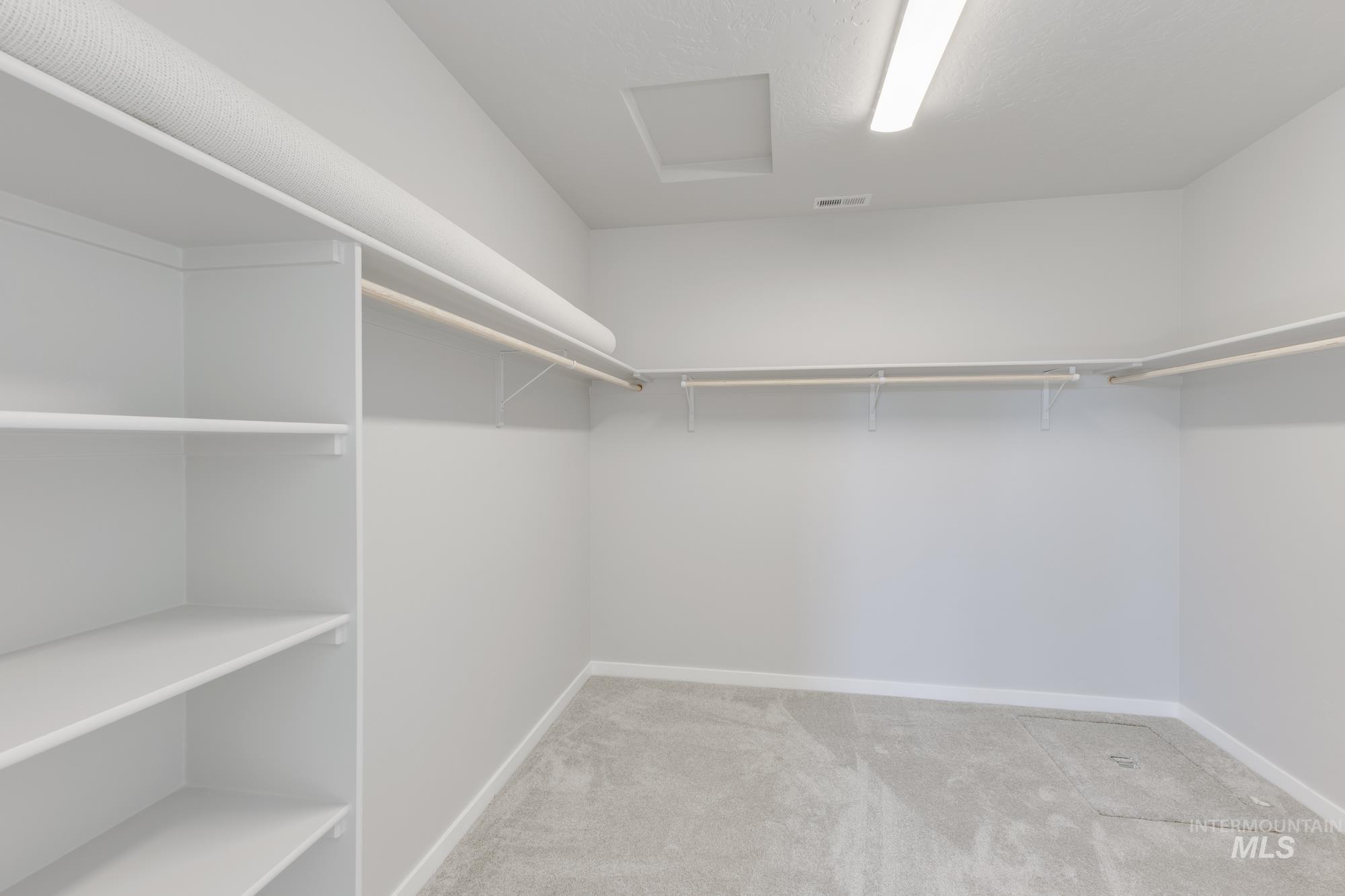 Walk in closet with light carpet and attic access