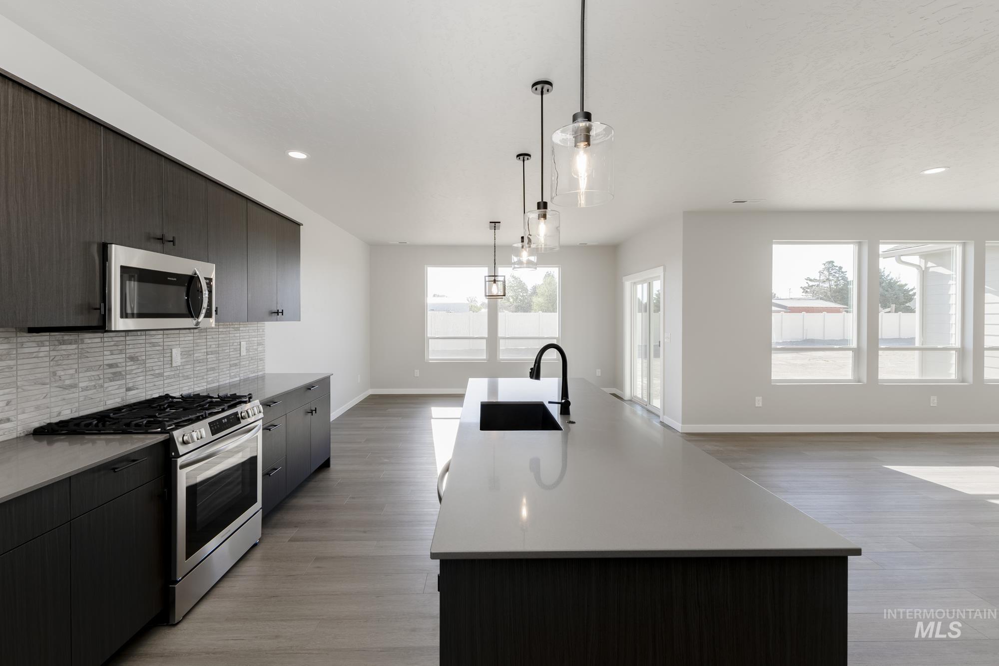 Kitchen with stainless steel appliances, tasteful backsplash, a kitchen island with sink, hanging light fixtures, and modern cabinets