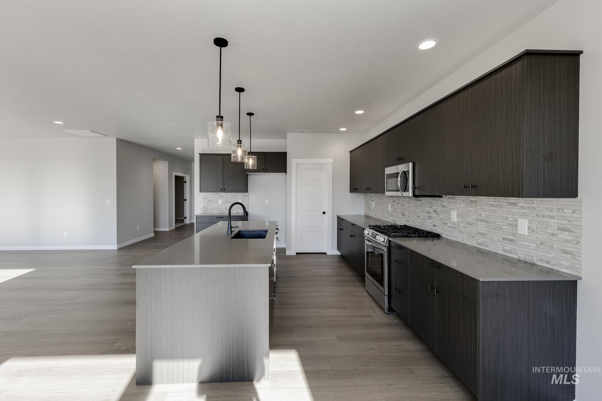 Kitchen featuring appliances with stainless steel finishes, hanging light fixtures, a kitchen island with sink, light wood-style floors, and recessed lighting