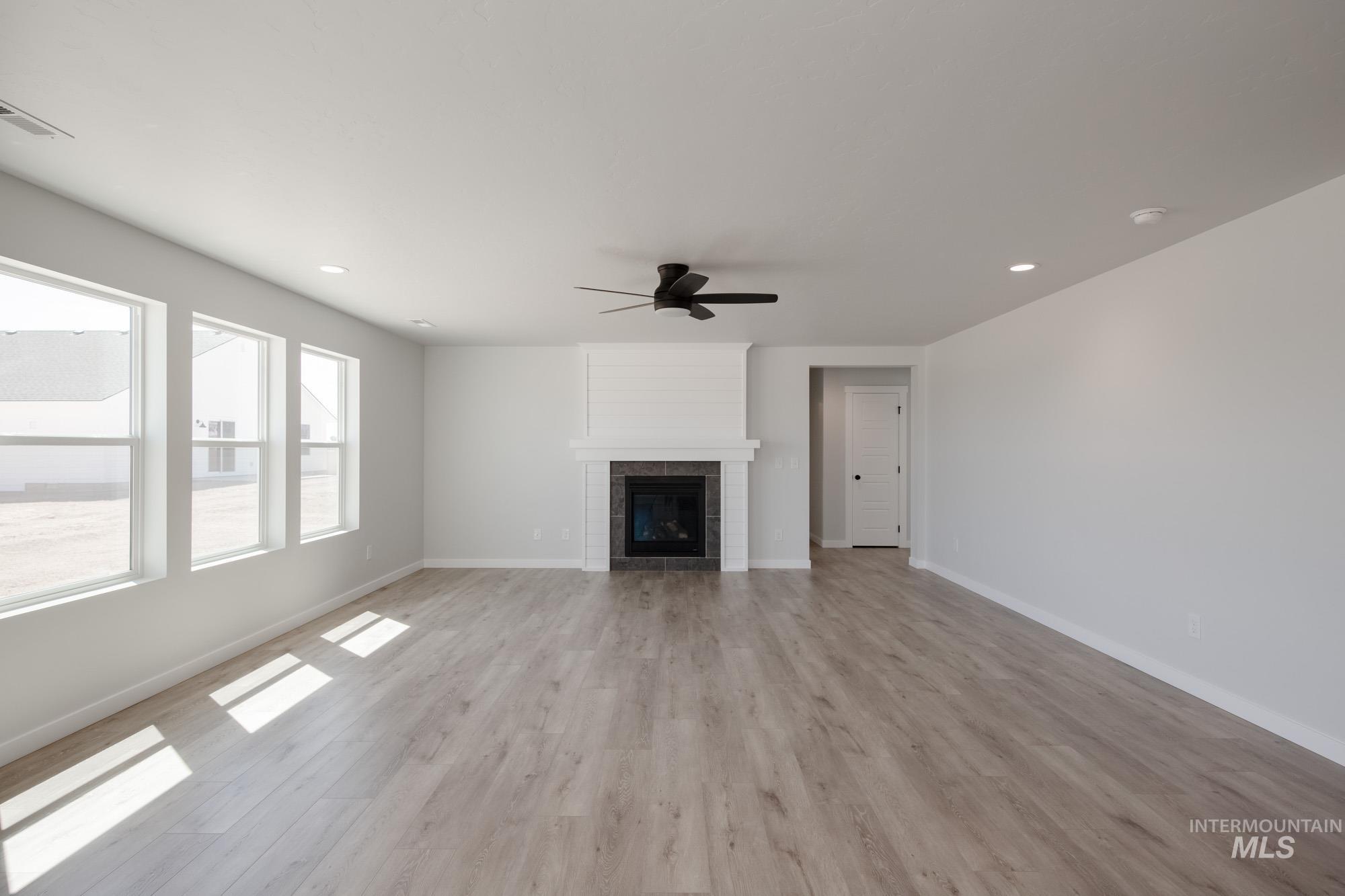 Unfurnished living room with light wood-type flooring, a tiled fireplace, a ceiling fan, and recessed lighting
