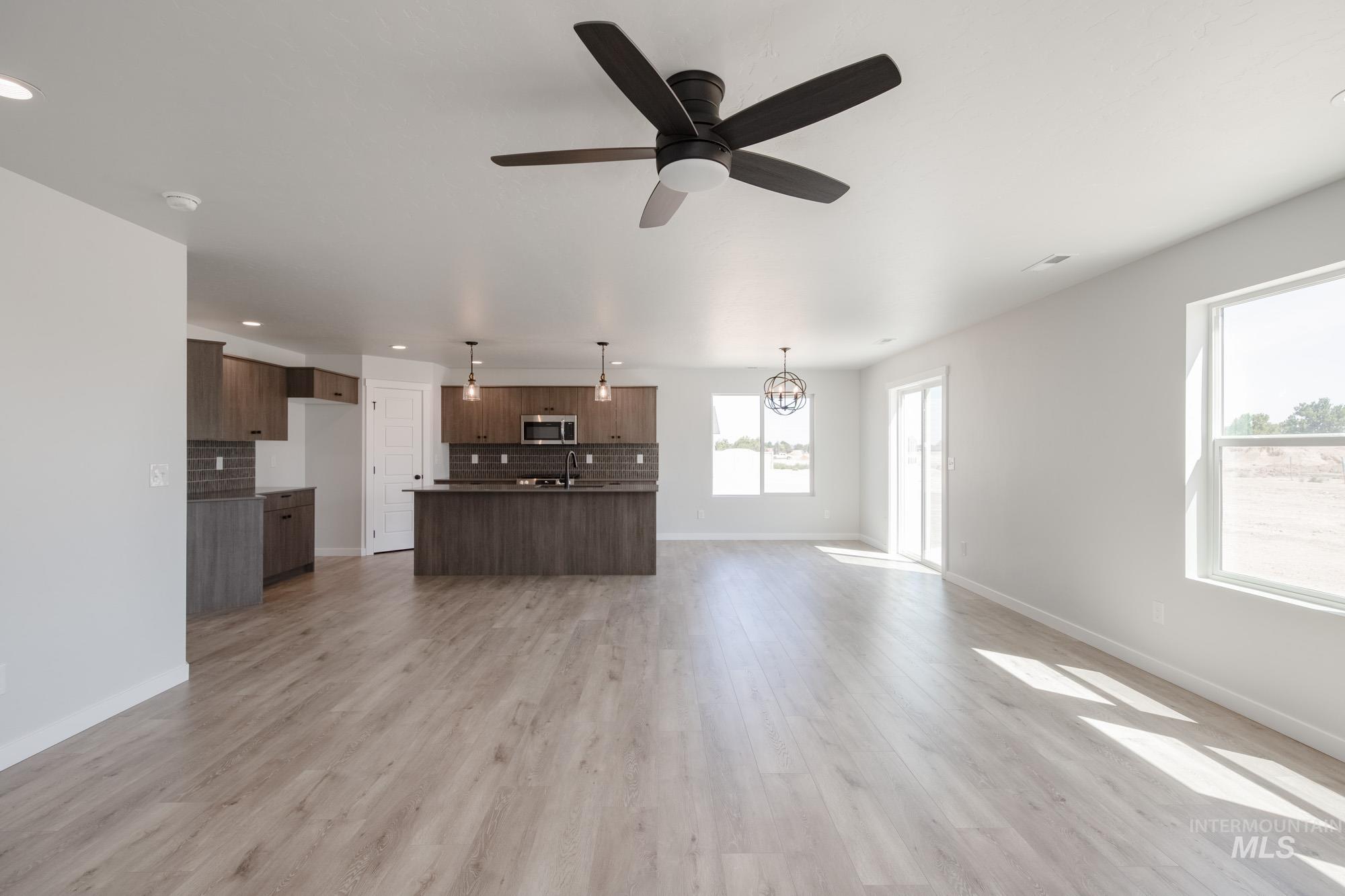 Unfurnished living room with ceiling fan, light wood-style floors, recessed lighting, and a chandelier