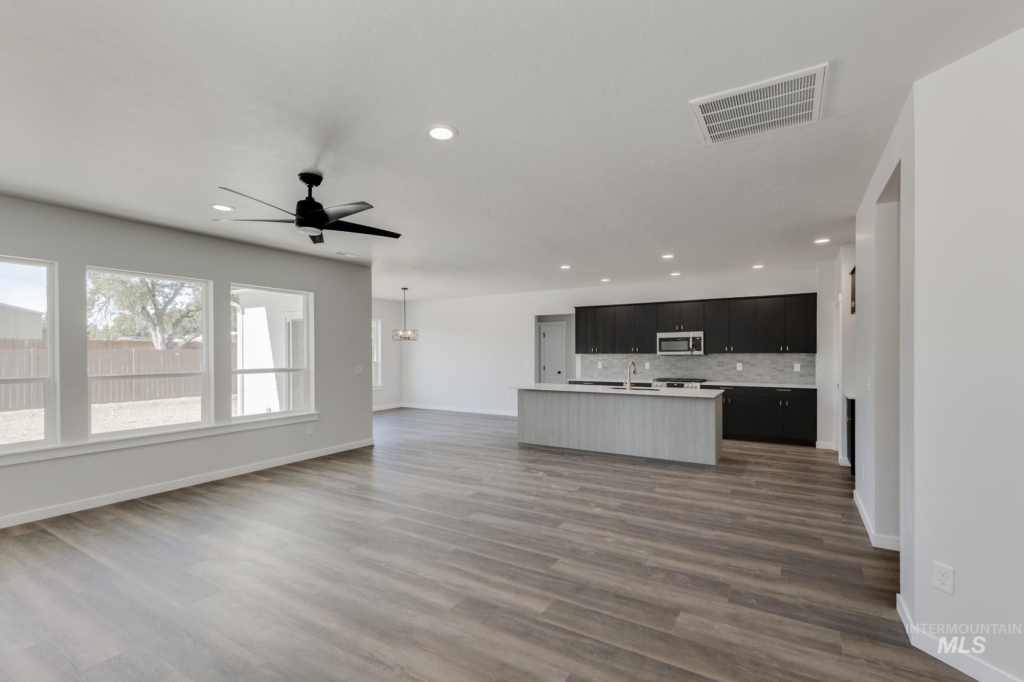 Kitchen featuring light countertops, open floor plan, recessed lighting, a kitchen island with sink, and dark cabinetry