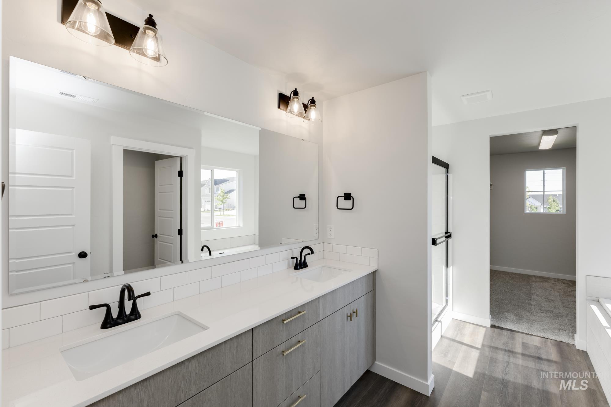 Bathroom featuring double vanity, healthy amount of natural light, dark wood-type flooring, and a stall shower