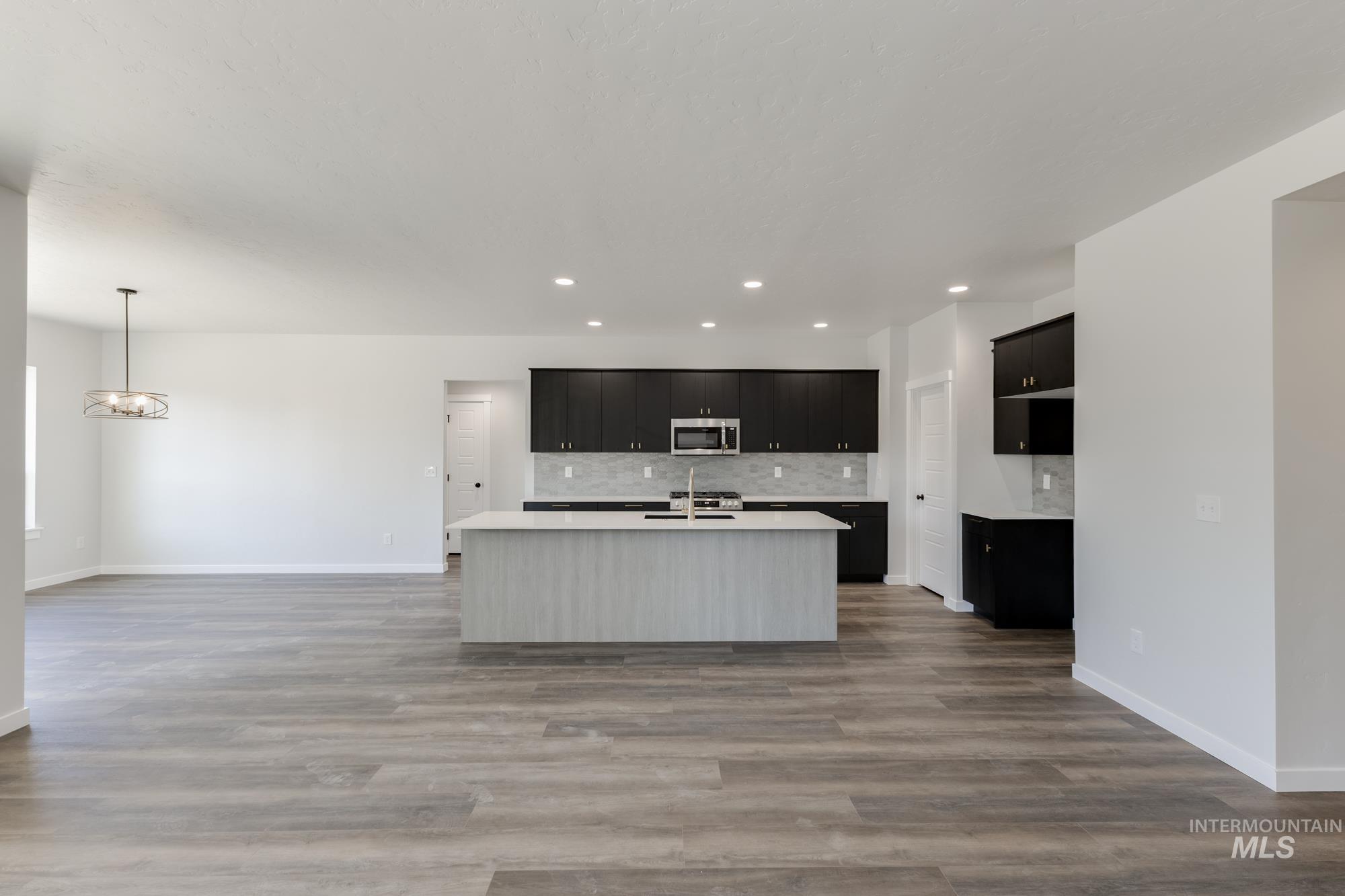 Kitchen featuring dark cabinetry, open floor plan, an island with sink, decorative backsplash, and recessed lighting