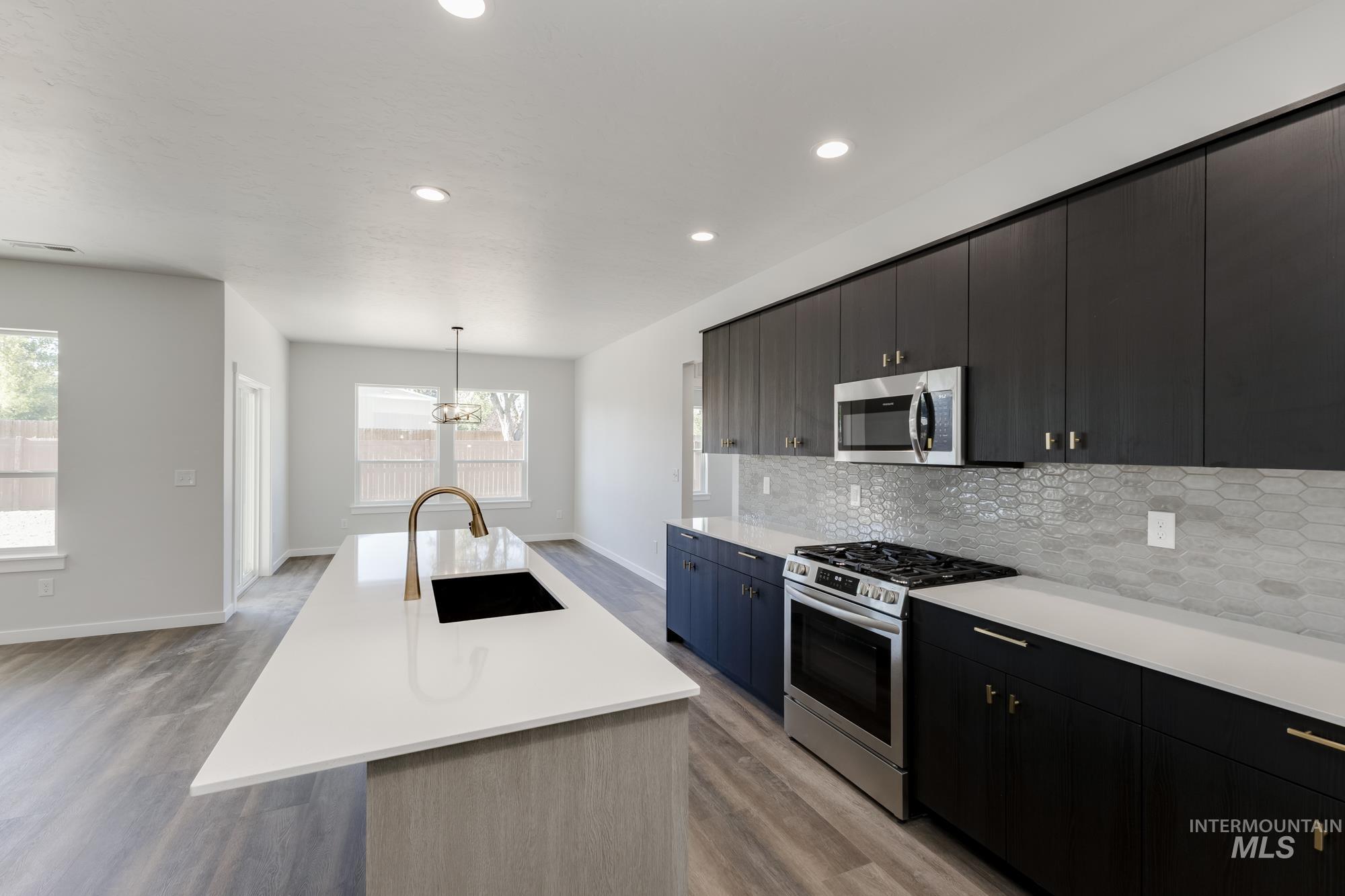 Kitchen with appliances with stainless steel finishes, decorative light fixtures, a center island with sink, tasteful backsplash, and recessed lighting