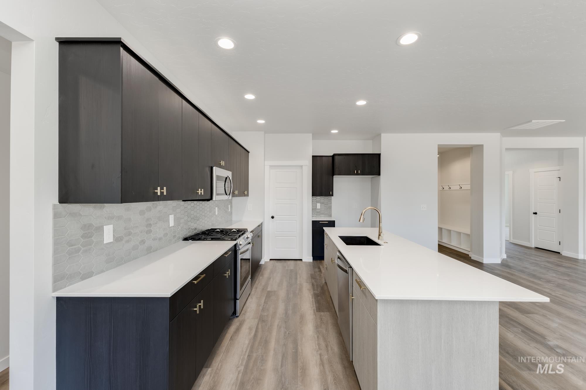 Kitchen with stainless steel appliances, backsplash, light wood finished floors, light stone counters, and a kitchen island with sink