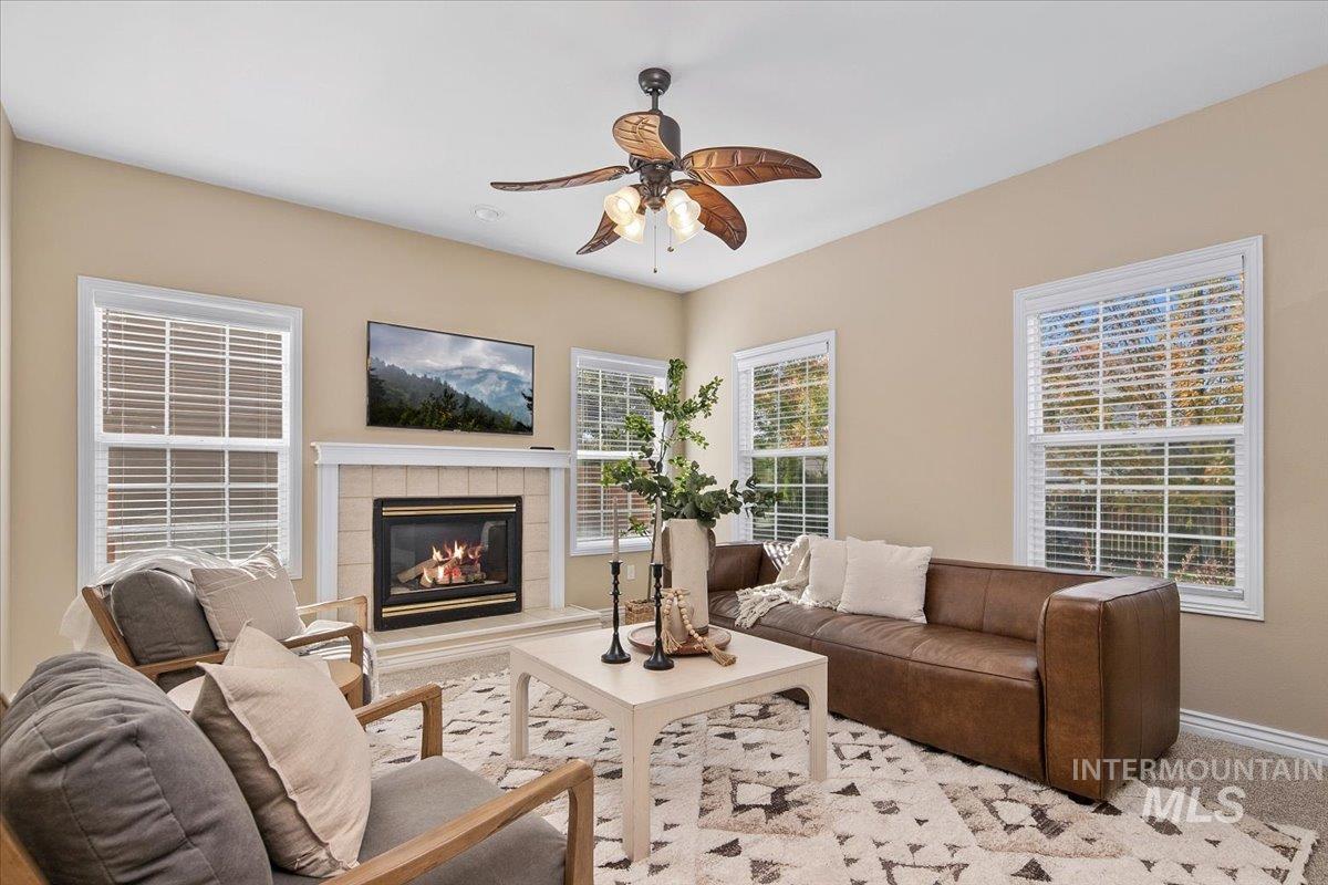 Carpeted living room with a tiled fireplace and ceiling fan