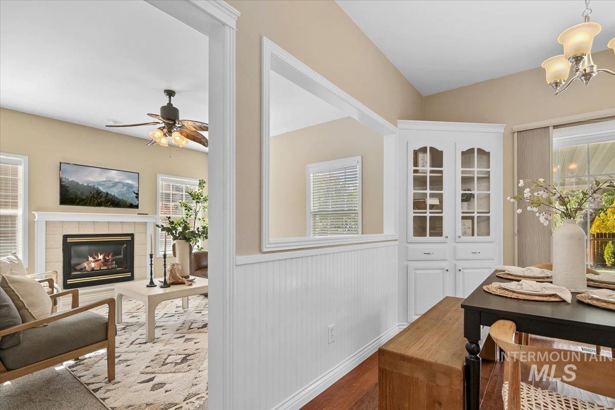 Dining area featuring a wainscoted wall, wood finished floors, a tile fireplace, a chandelier, and a ceiling fan