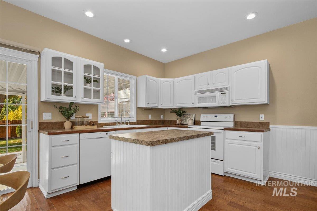 Kitchen with glass insert cabinets, white appliances, white cabinets, dark countertops, and dark wood-style flooring