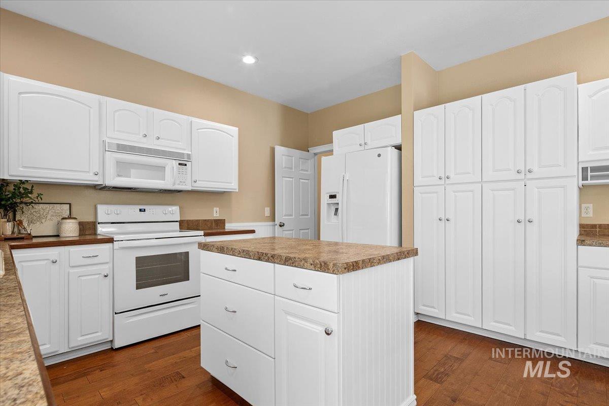Kitchen with white appliances, a kitchen island, white cabinetry, and recessed lighting