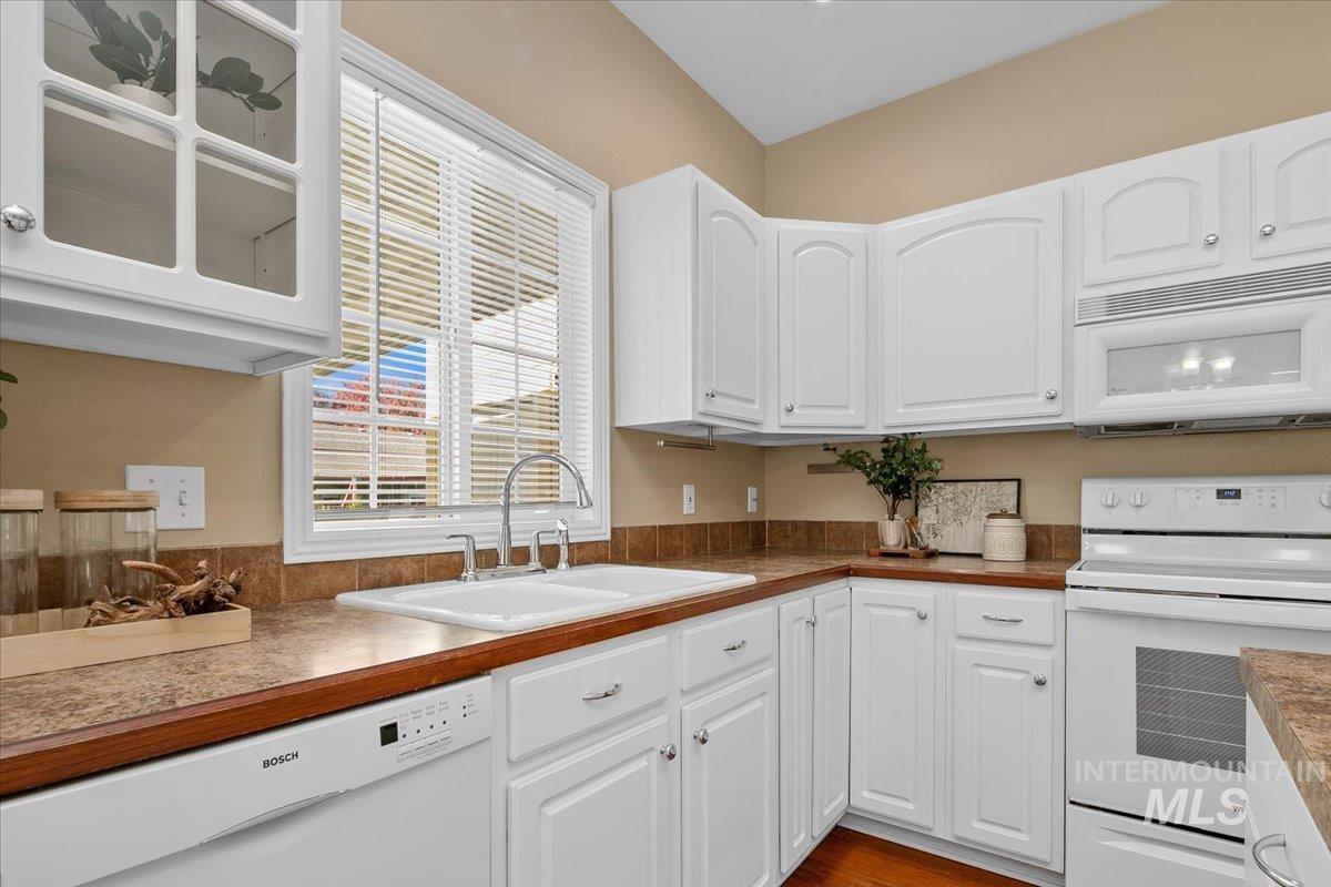 Kitchen featuring white appliances, white cabinets, glass insert cabinets, and dark wood-style flooring