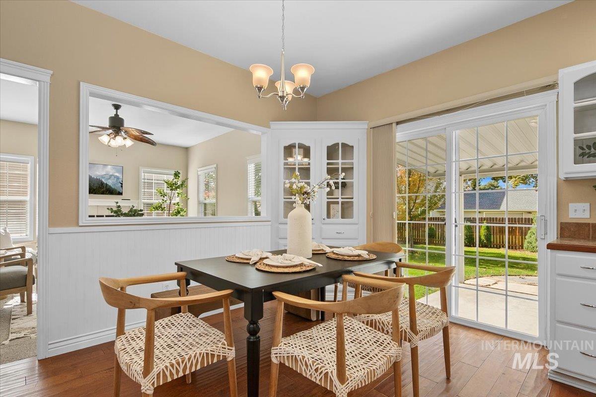 Dining area featuring light wood-style flooring, healthy amount of natural light, wainscoting, ceiling fan, and a chandelier