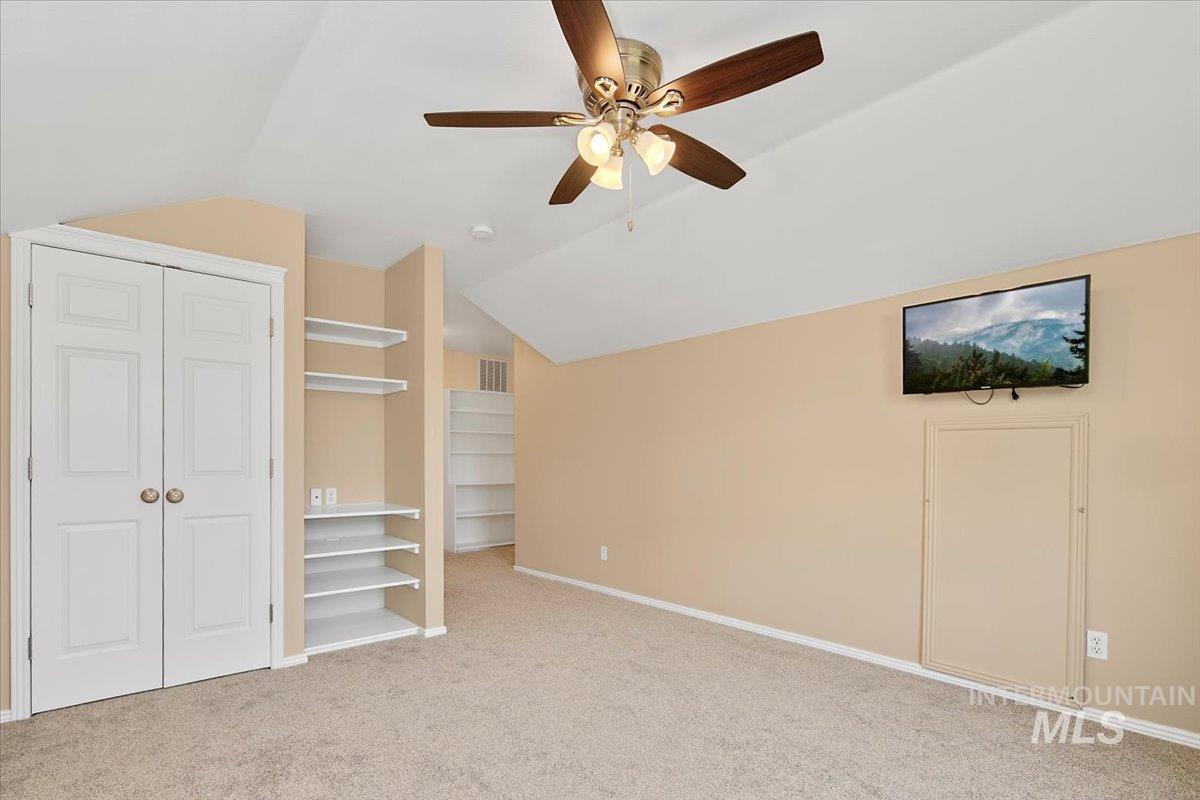 Unfurnished bedroom with vaulted ceiling, light colored carpet, and a ceiling fan
