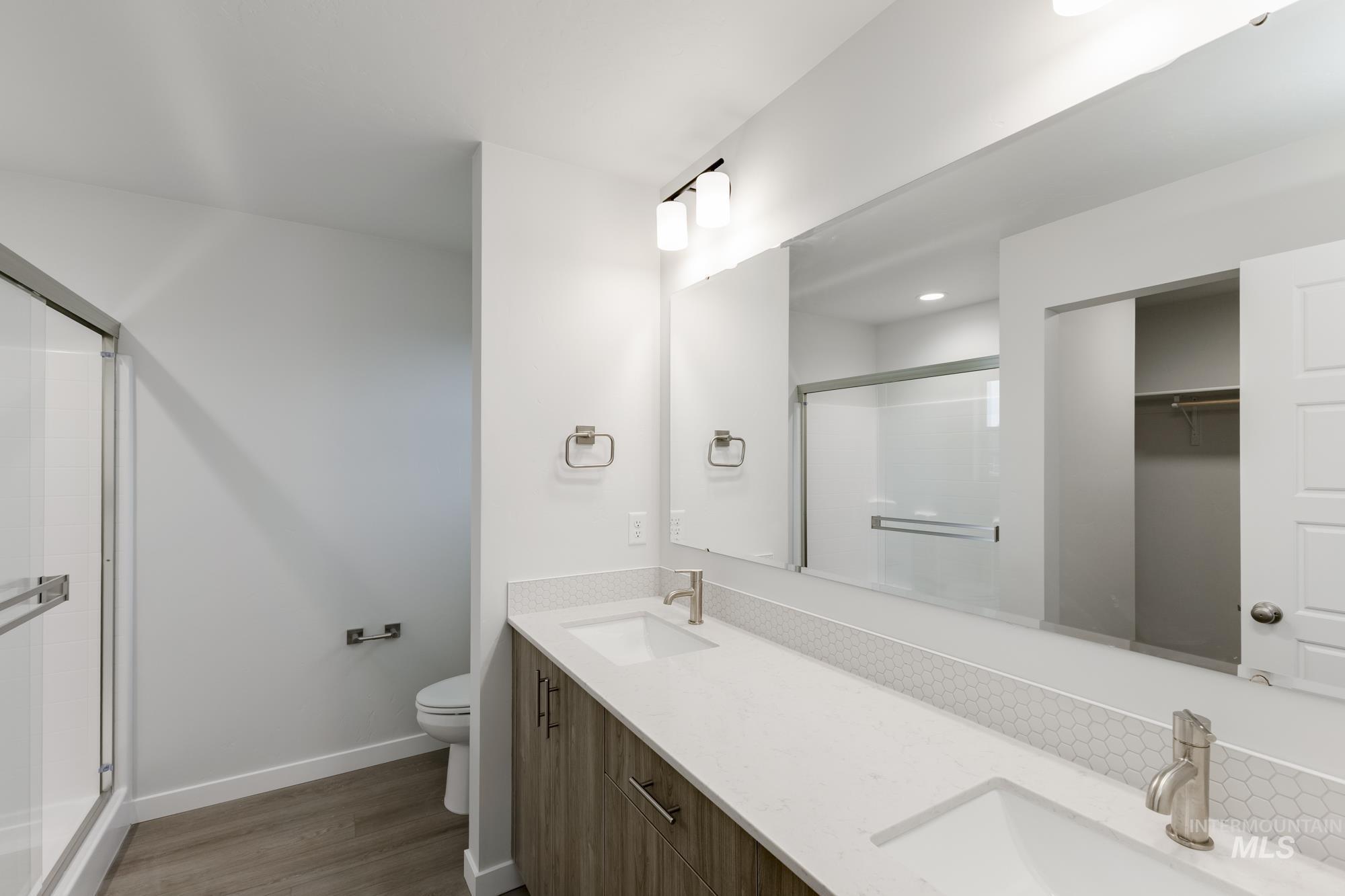 Full bath with double vanity, a stall shower, dark wood-type flooring, and a spacious closet