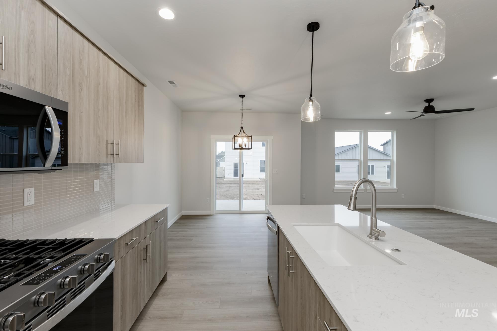 Kitchen featuring decorative light fixtures, light brown cabinetry, modern cabinets, stainless steel appliances, and light stone countertops