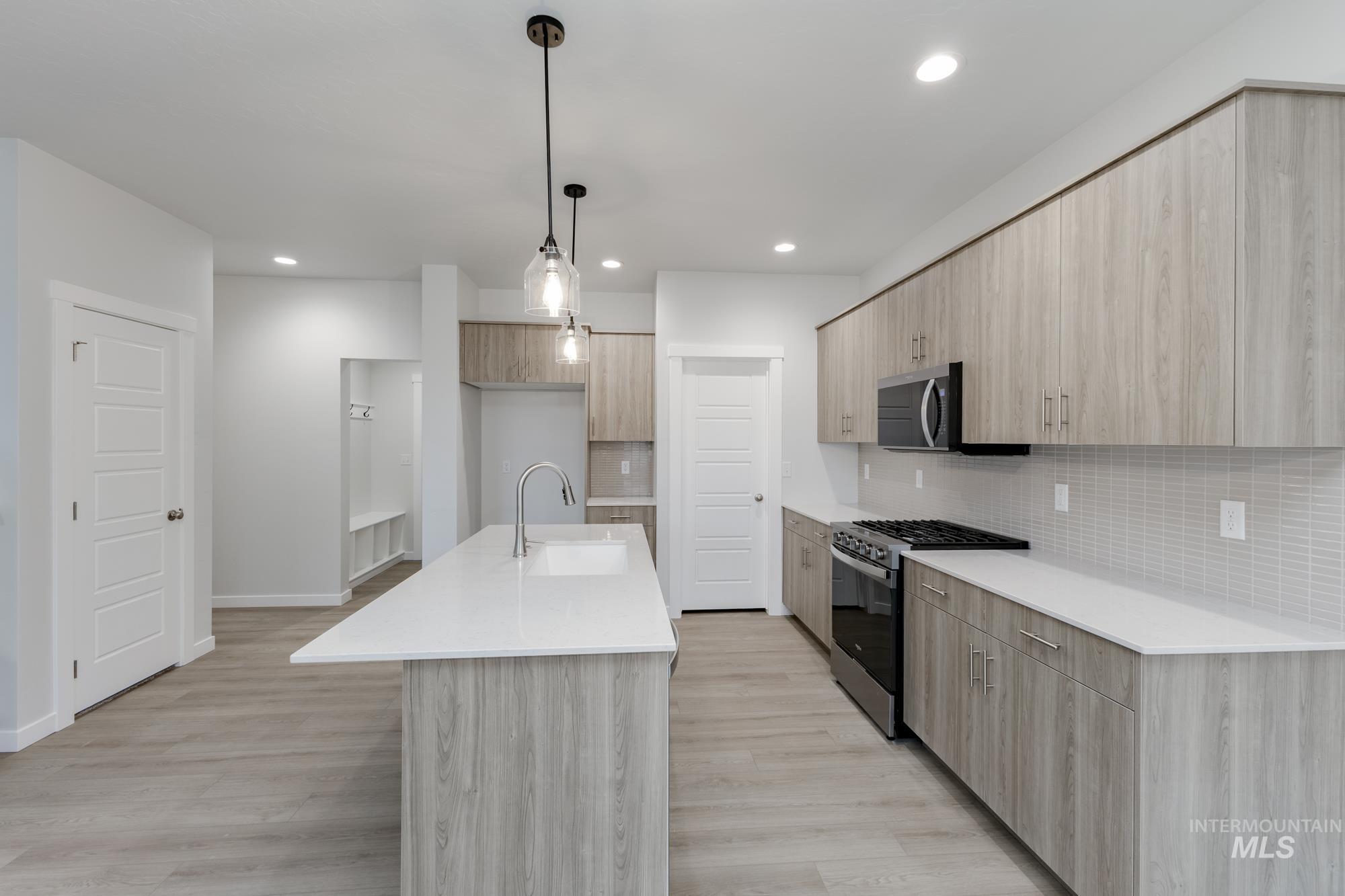 Kitchen featuring light stone counters, modern cabinets, appliances with stainless steel finishes, light brown cabinets, and pendant lighting