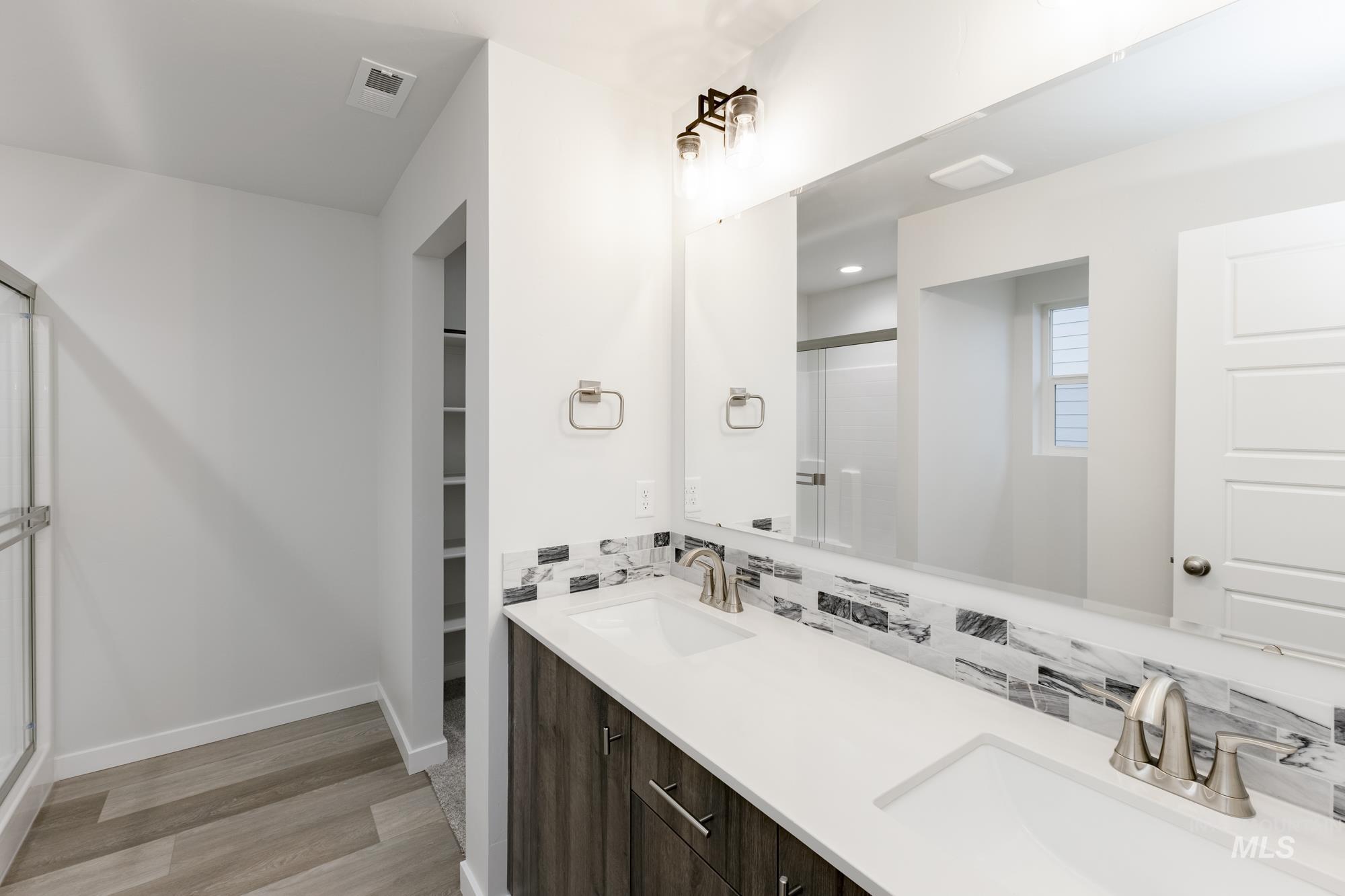 Full bathroom with a stall shower, double vanity, a spacious closet, and light wood-style flooring