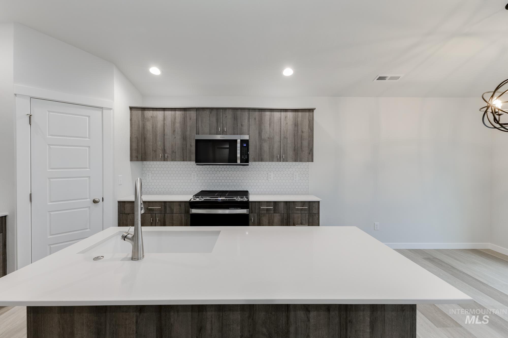 Kitchen featuring dark brown cabinets, appliances with stainless steel finishes, a center island with sink, tasteful backsplash, and recessed lighting