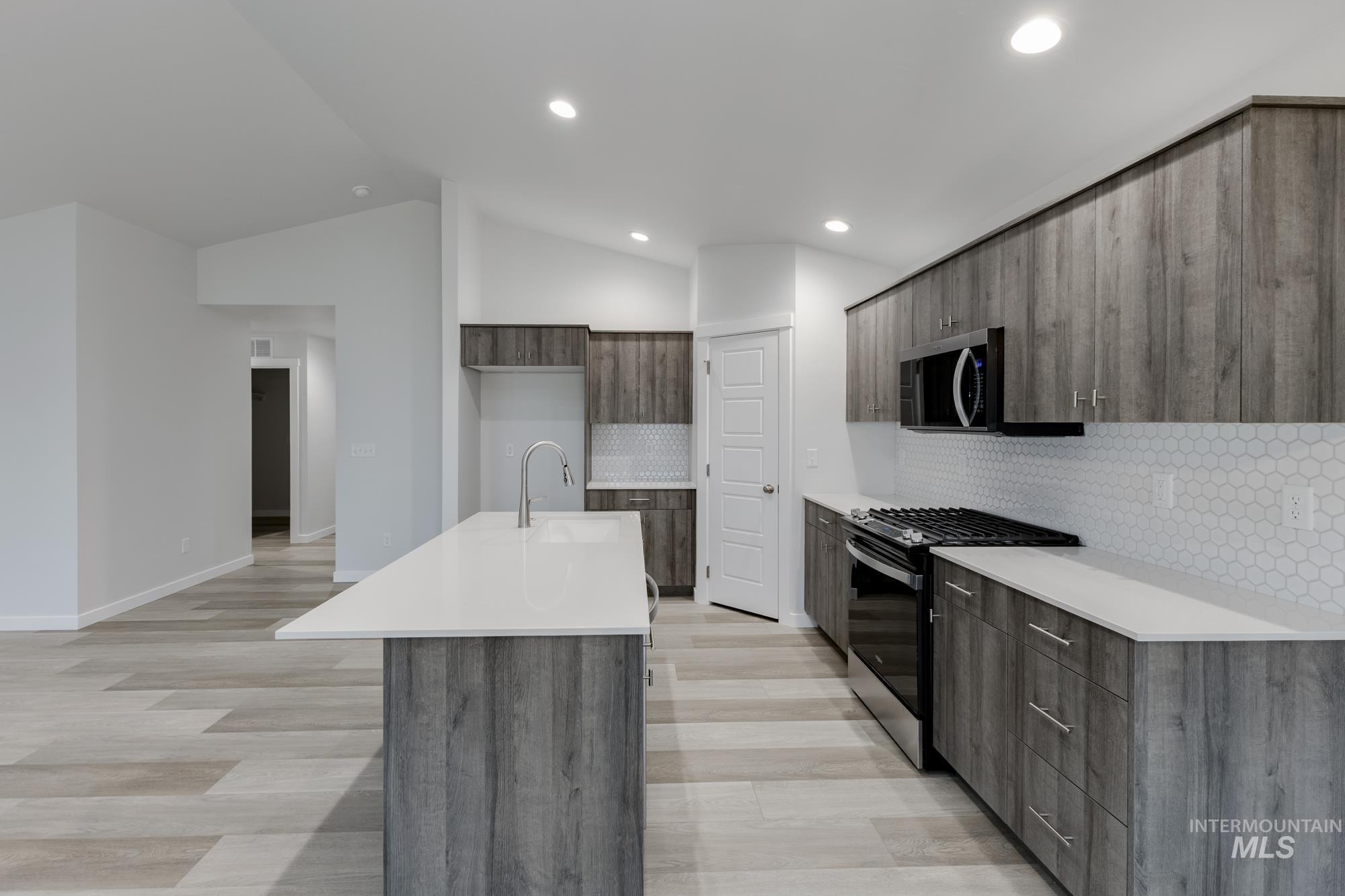 Kitchen featuring appliances with stainless steel finishes, modern cabinets, an island with sink, light stone countertops, and vaulted ceiling