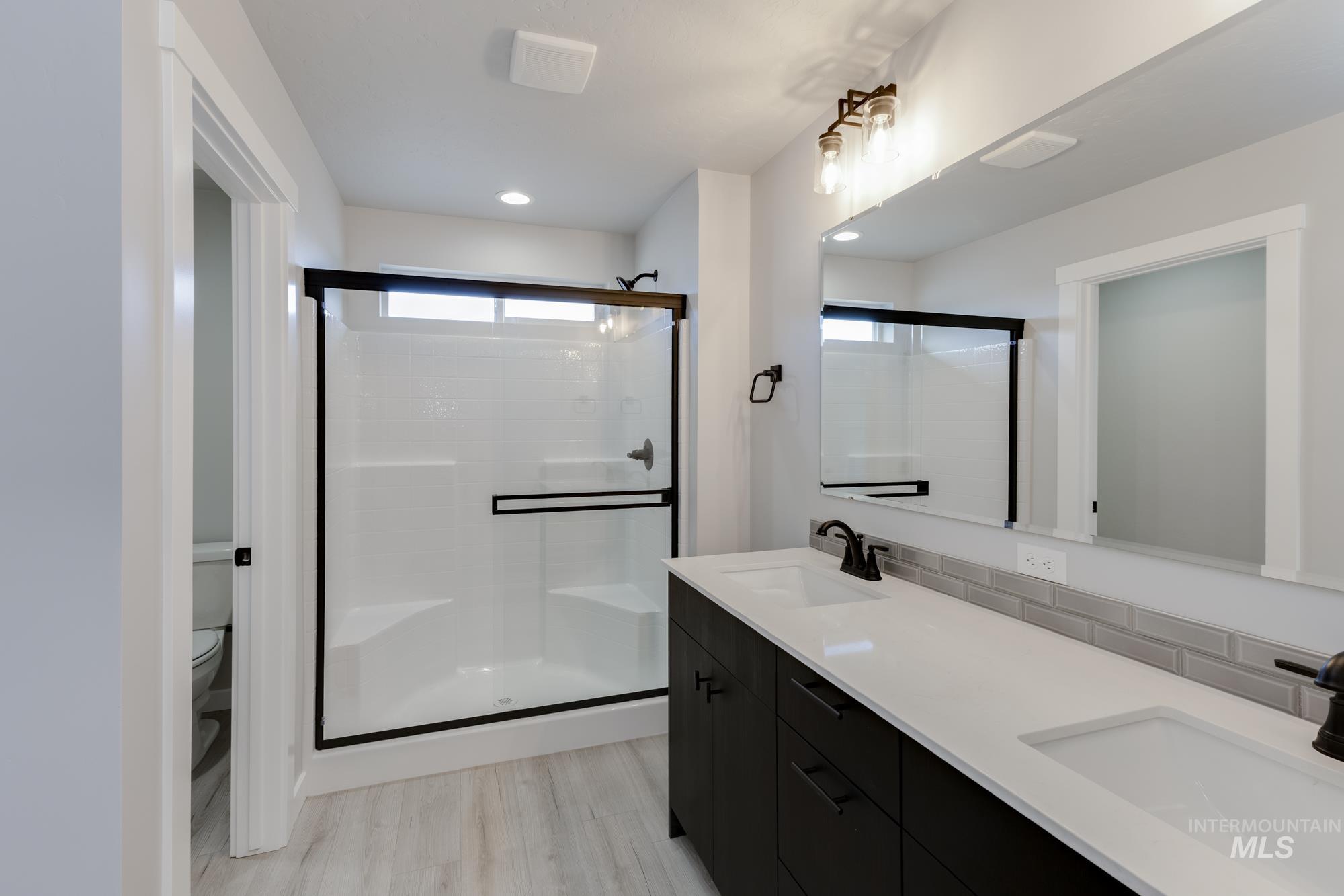 Full bath featuring a shower stall, double vanity, plenty of natural light, and light wood-style flooring