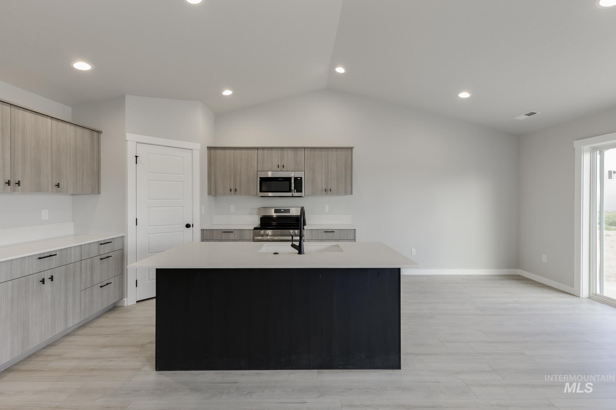 Kitchen with an island with sink, stainless steel appliances, recessed lighting, light wood-style flooring, and light stone countertops
