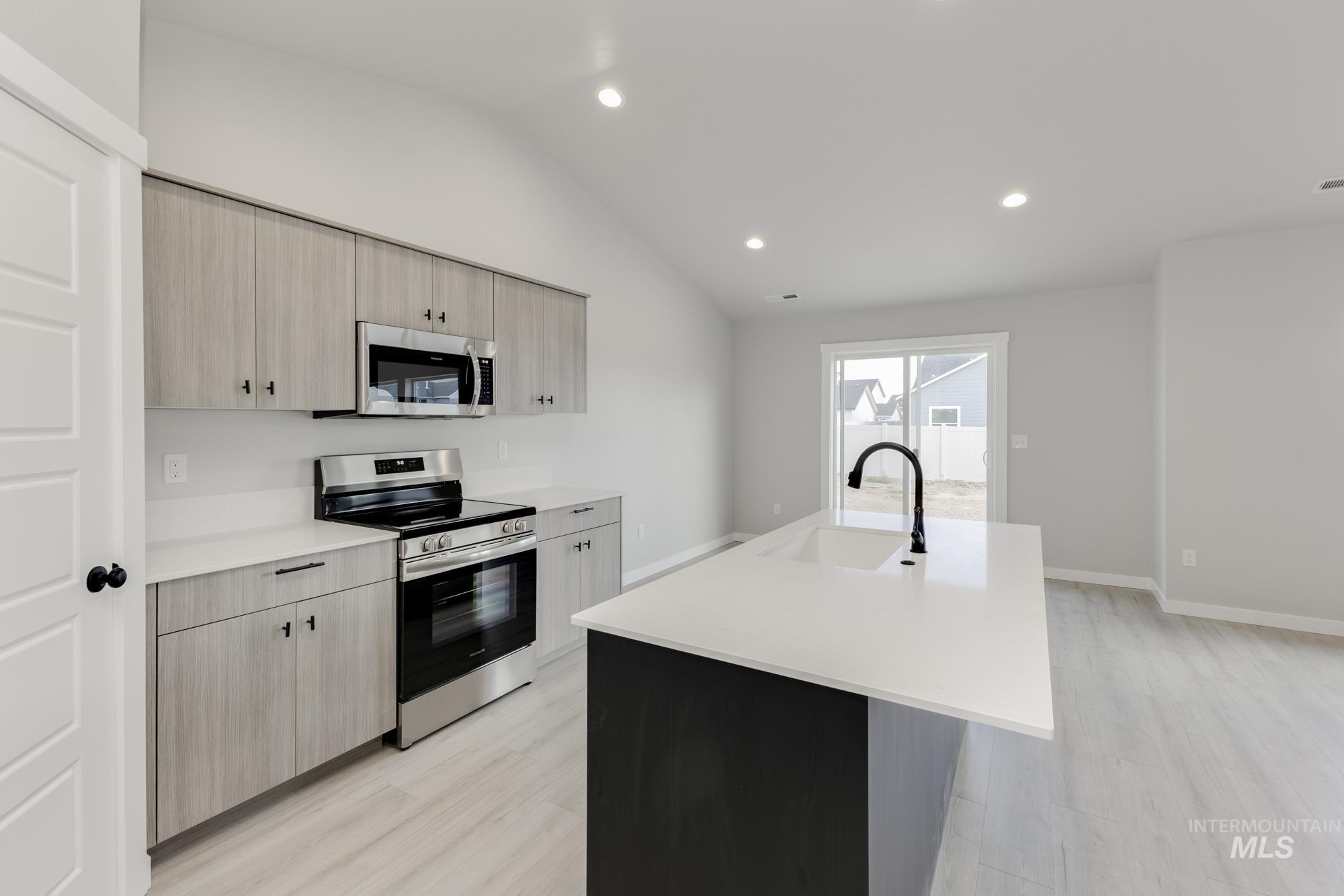 Kitchen with light brown cabinetry, stainless steel appliances, vaulted ceiling, a center island with sink, and recessed lighting