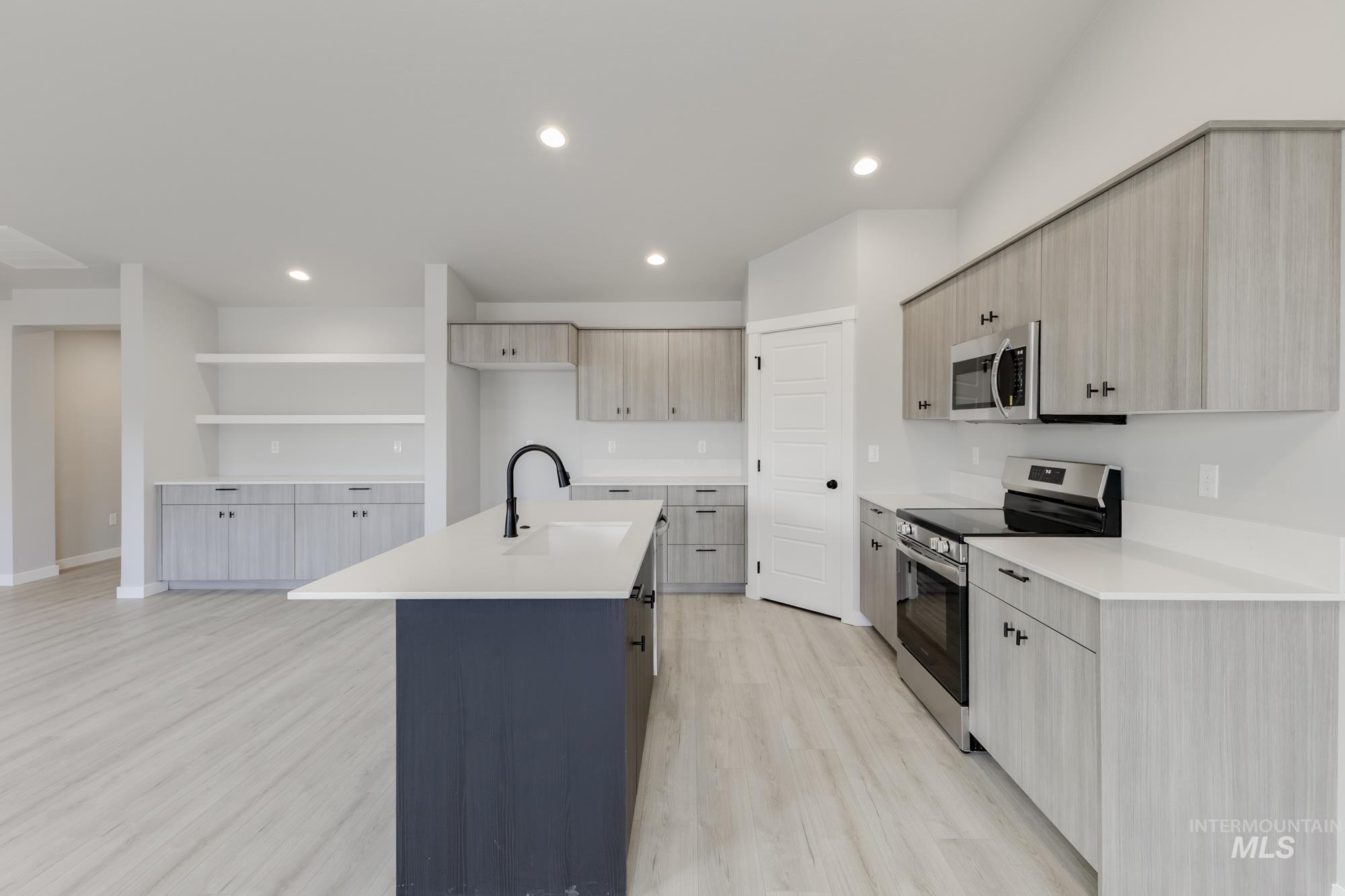 Kitchen with appliances with stainless steel finishes, a center island with sink, light wood-type flooring, open shelves, and modern cabinets