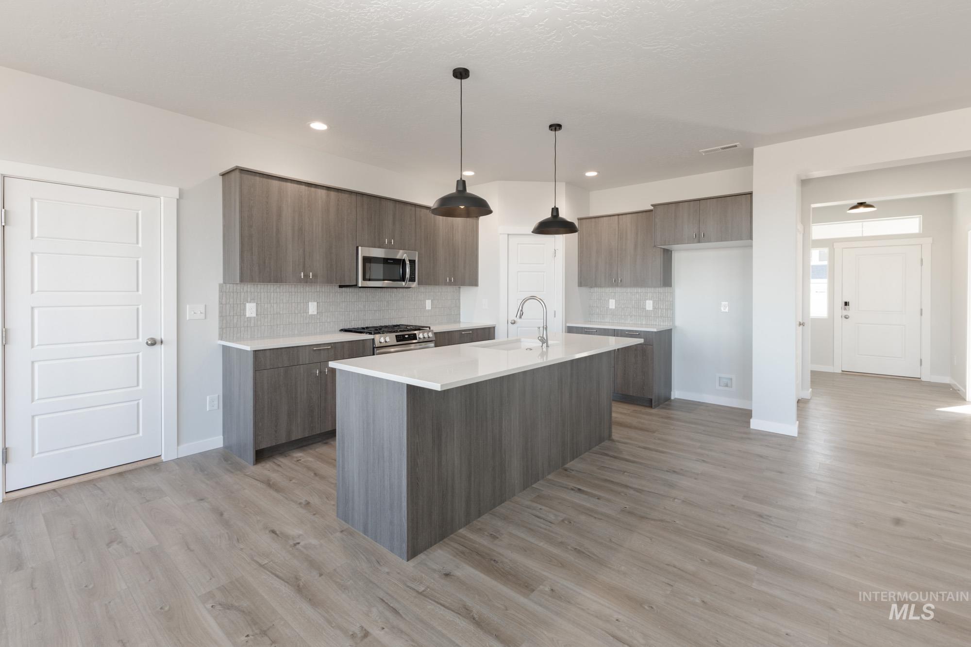 Kitchen with modern cabinets, a kitchen island with sink, backsplash, appliances with stainless steel finishes, and hanging light fixtures