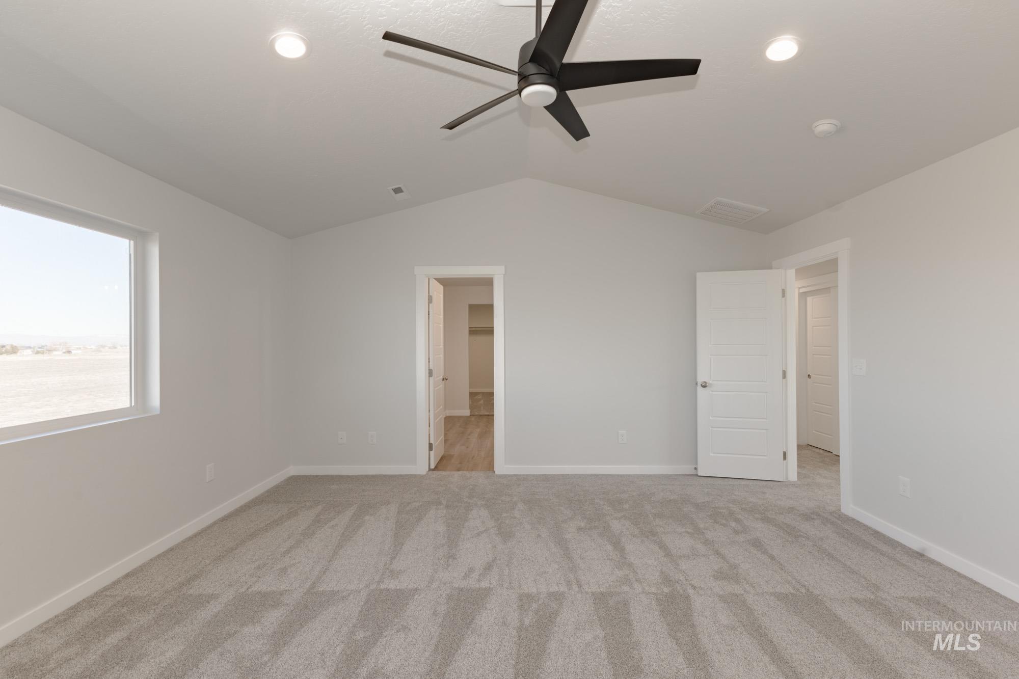 Unfurnished bedroom featuring lofted ceiling, light colored carpet, a ceiling fan, and connected bathroom