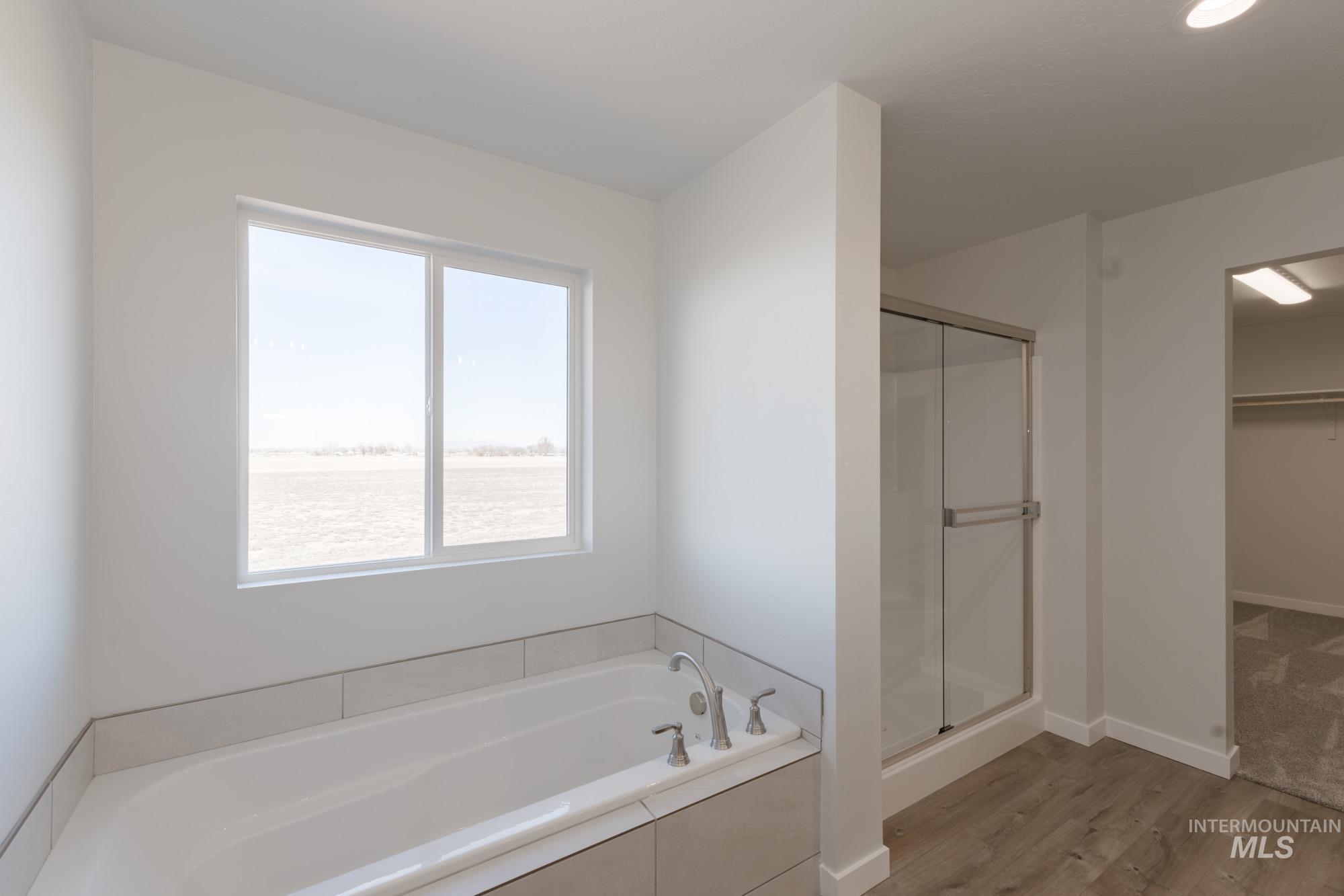 Bathroom with a shower stall, a bath, light wood finished floors, and a walk in closet