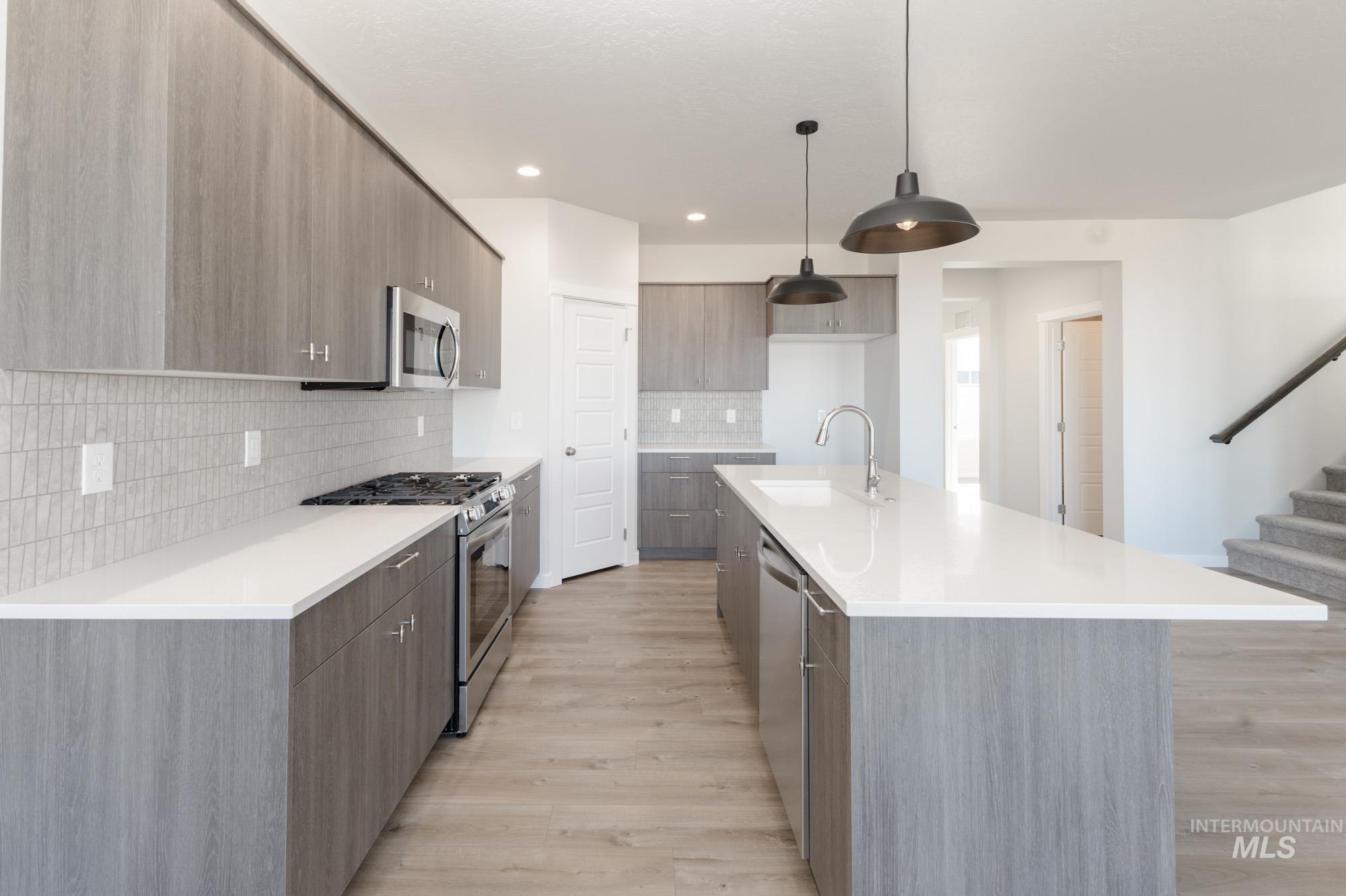 Kitchen featuring modern cabinets, stainless steel appliances, decorative light fixtures, an island with sink, and light wood-type flooring