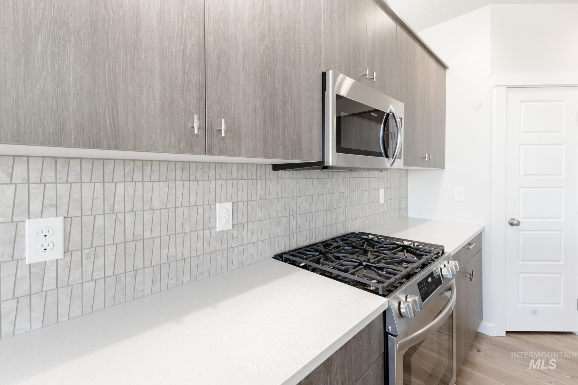 Kitchen with appliances with stainless steel finishes, modern cabinets, light wood-style flooring, and tasteful backsplash
