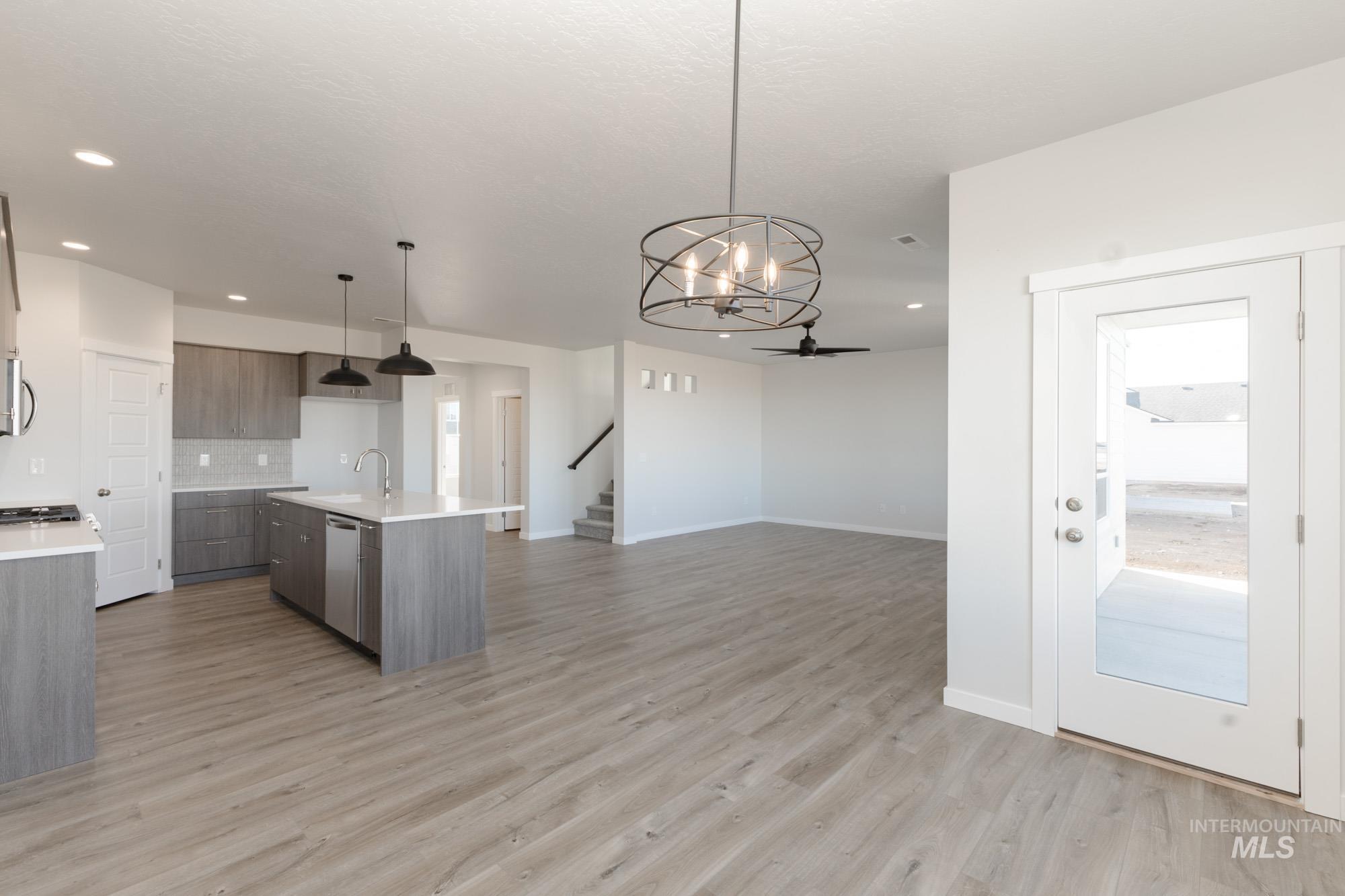 Kitchen featuring a chandelier, a center island with sink, decorative light fixtures, light wood-style flooring, and tasteful backsplash