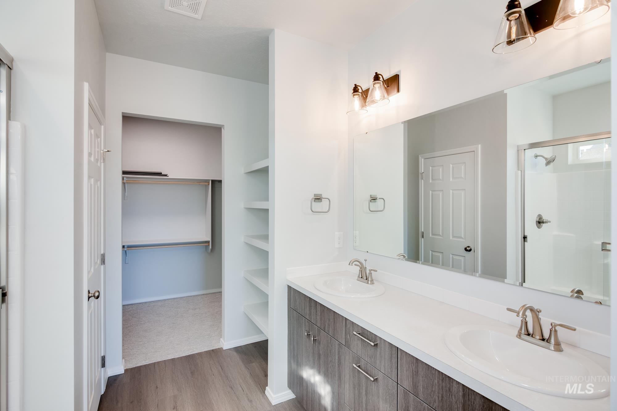 Bathroom with a walk in closet, a stall shower, double vanity, and light wood-style flooring