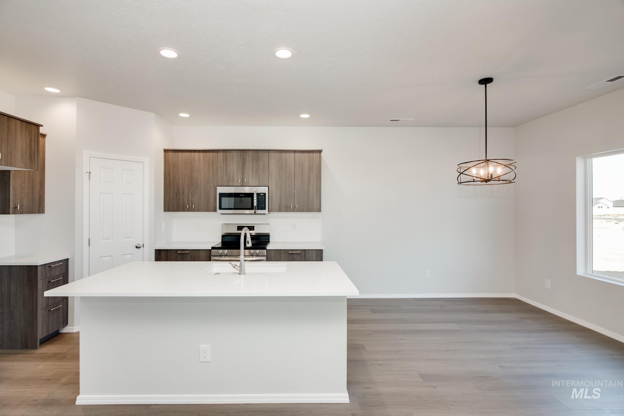 Kitchen featuring a center island with sink, pendant lighting, light wood finished floors, appliances with stainless steel finishes, and light stone counters