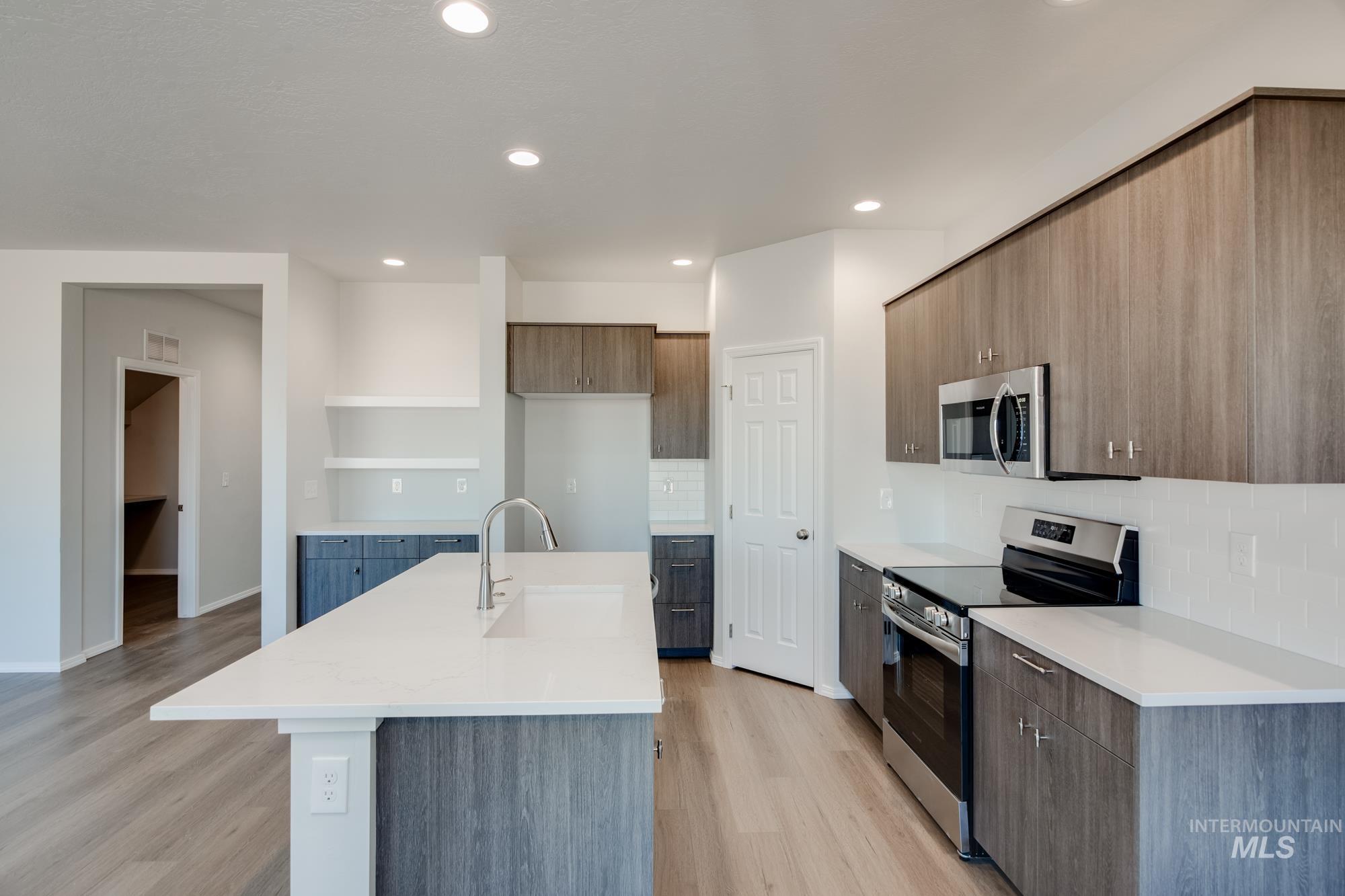 Kitchen featuring appliances with stainless steel finishes, modern cabinets, decorative backsplash, an island with sink, and light wood-style flooring