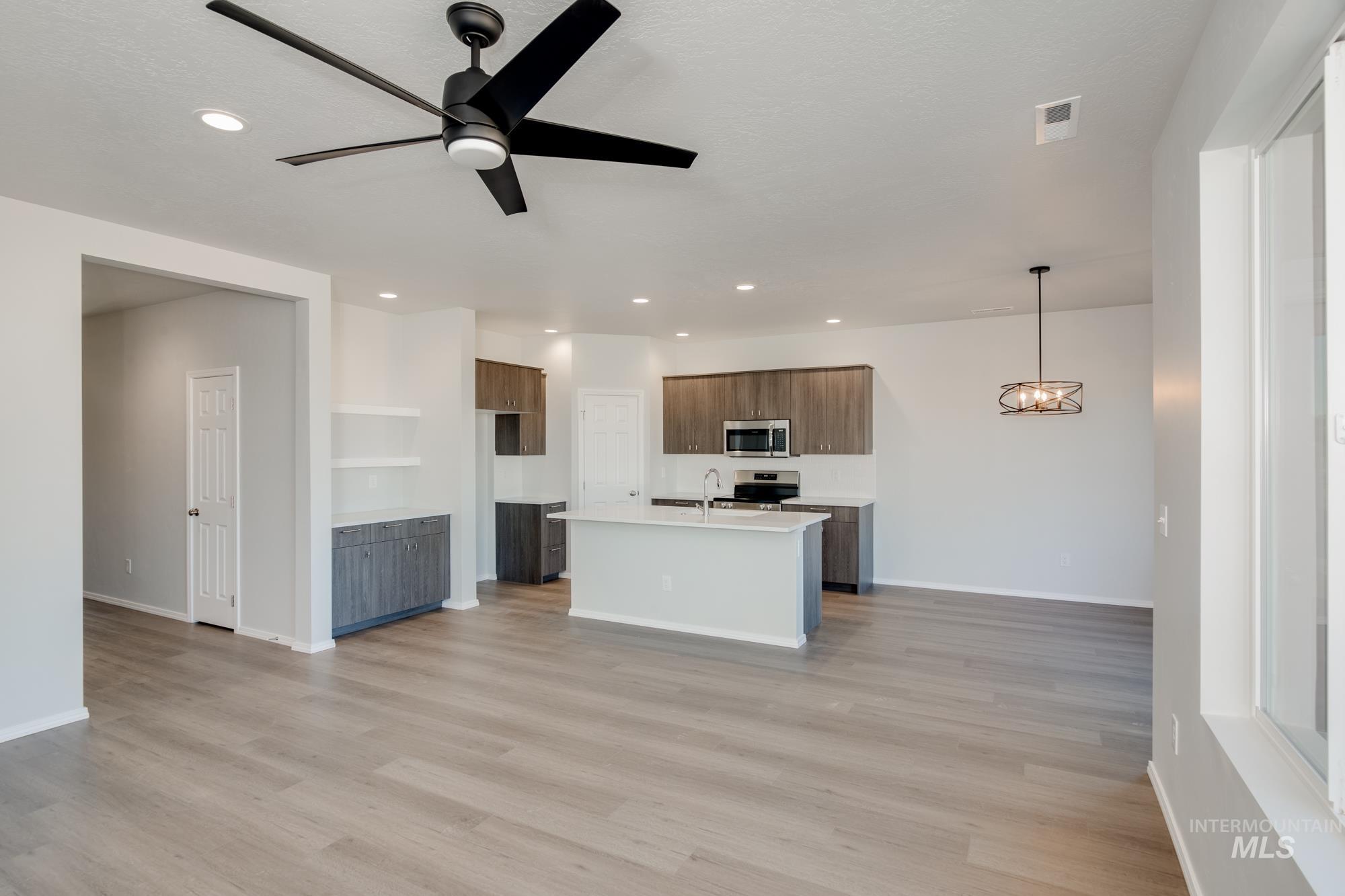Kitchen featuring open floor plan, ceiling fan, a kitchen island with sink, light wood-style floors, and stainless steel appliances