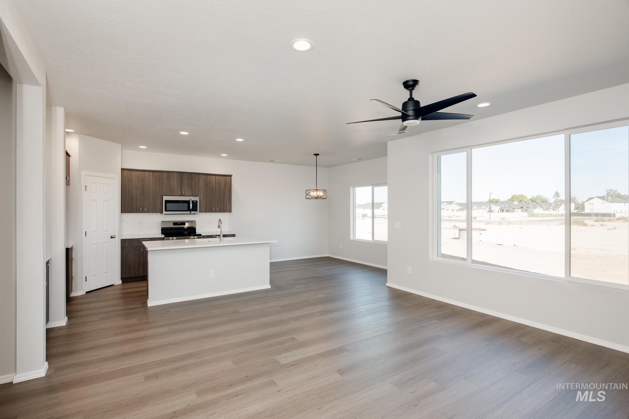 Kitchen featuring dark brown cabinetry, open floor plan, a center island with sink, decorative light fixtures, and appliances with stainless steel finishes