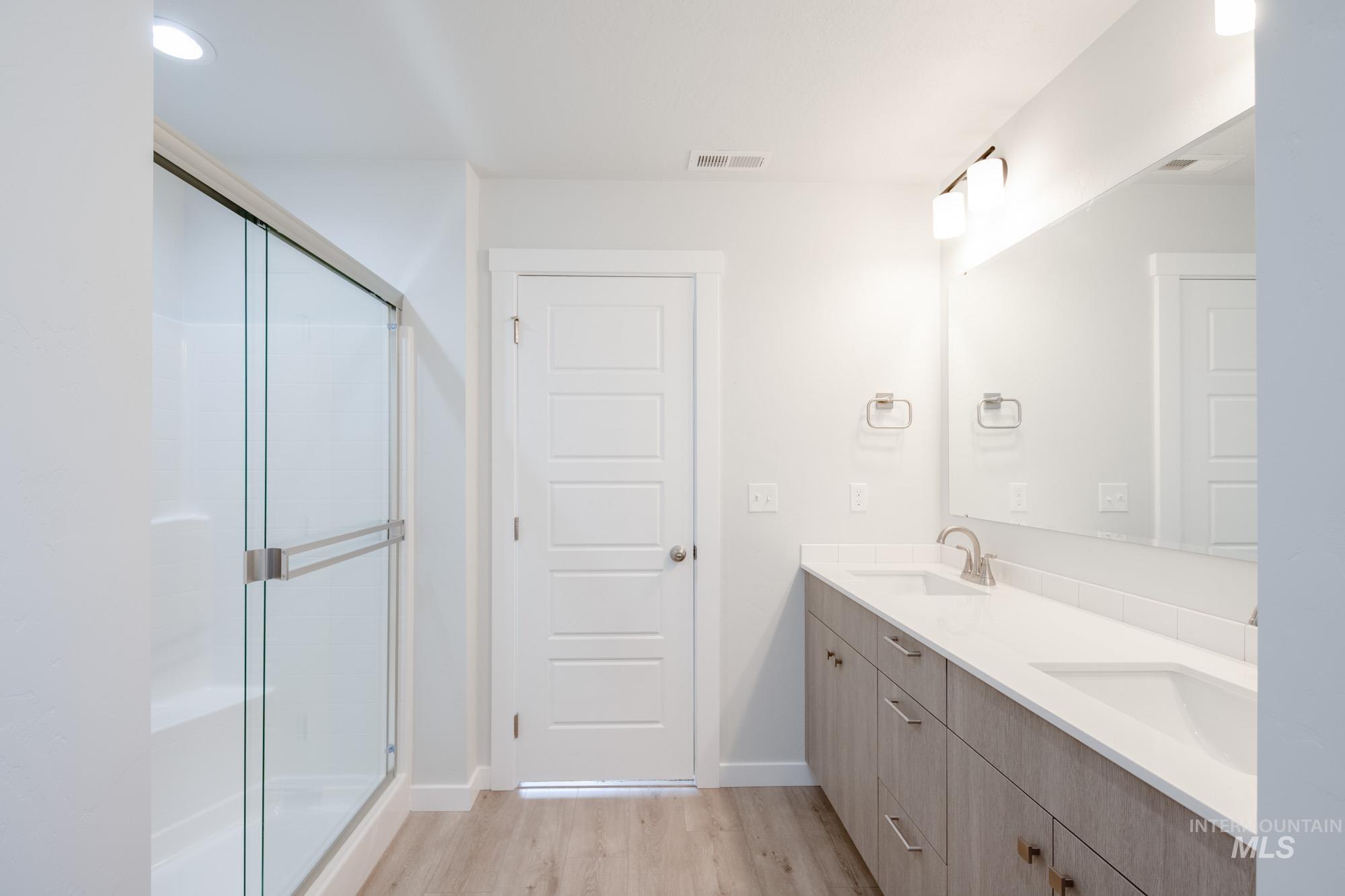 Bathroom featuring light wood-style floors, double vanity, a shower stall, and recessed lighting