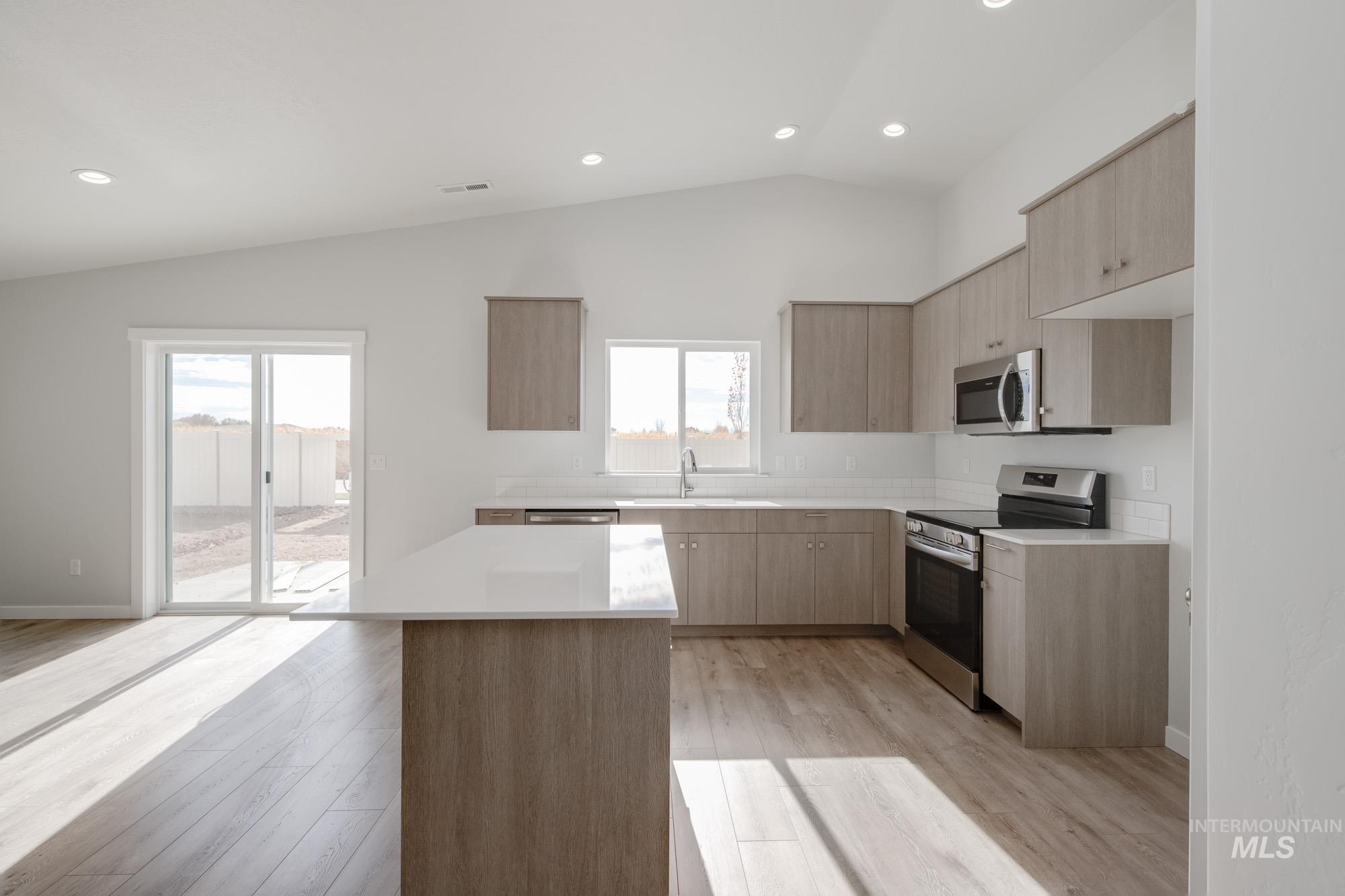 Kitchen featuring modern cabinets, stainless steel appliances, light wood-style flooring, vaulted ceiling, and recessed lighting
